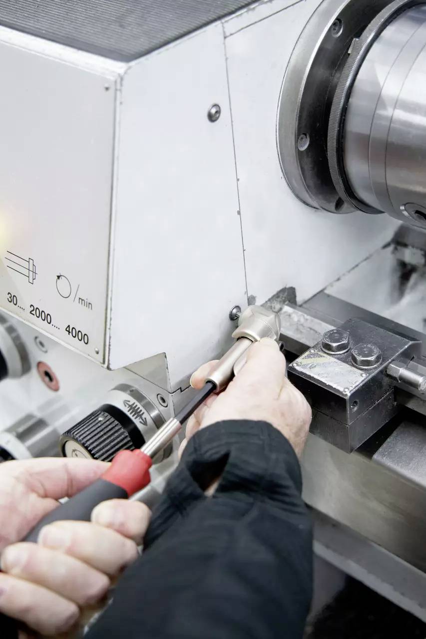 Eine Person, die eine Metallkehrmaschine einstellt und sich auf die Bedienelemente konzentriert, was auf eine Einrichtungs- oder Wartungsaktivität mit präziser manueller Handhabung hindeutet.