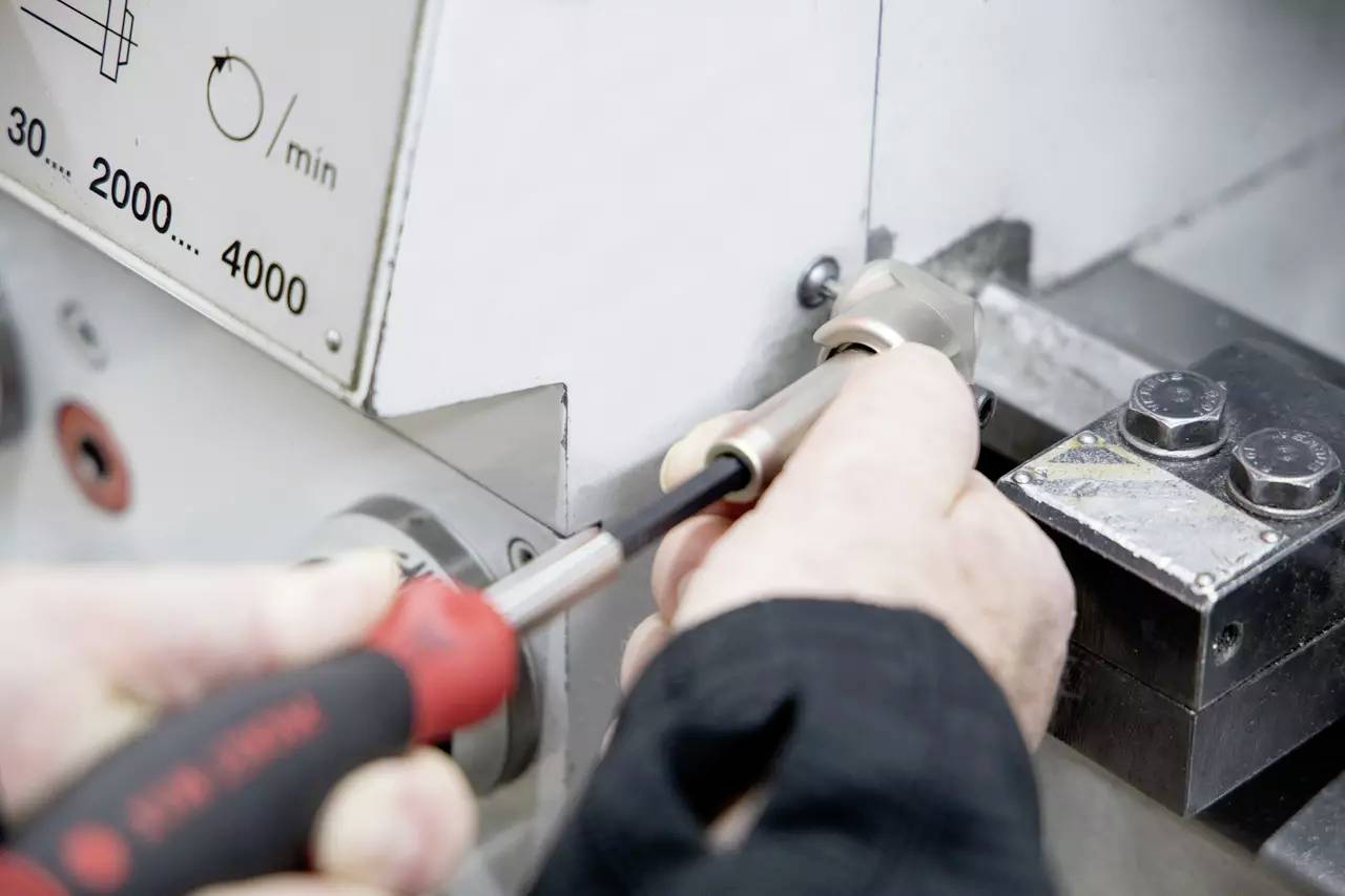 Eine Person verwendet einen Schraubendreher, um eine Maschine einzustellen und konzentriert sich dabei auf eine Komponente in der Nähe eines Bedienfelds mit Geschwindigkeitseinstellungen, die mit „0/min