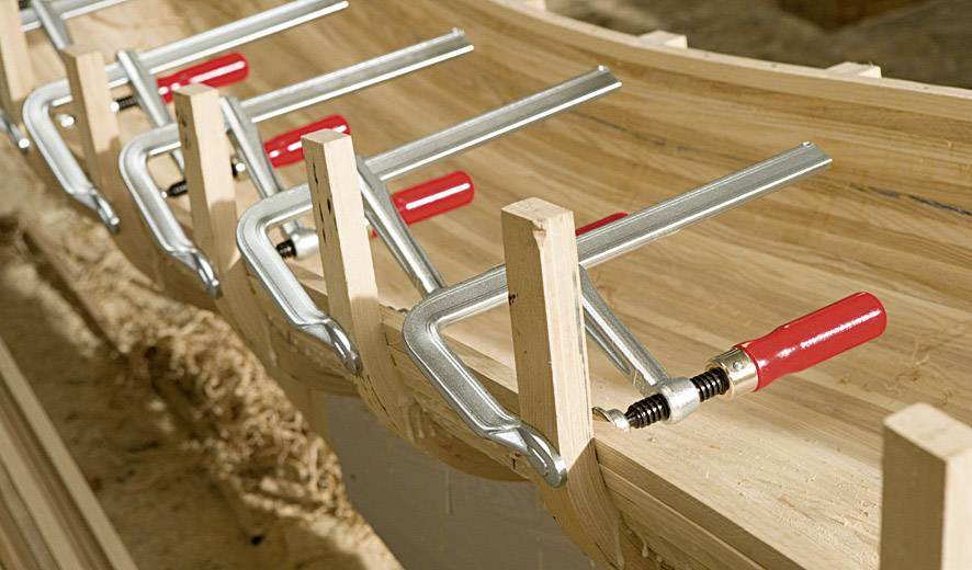 Mehrere Schraubzwingen halten gebogene Holzplanken zusammen, die für den Bau verwendet werden.
