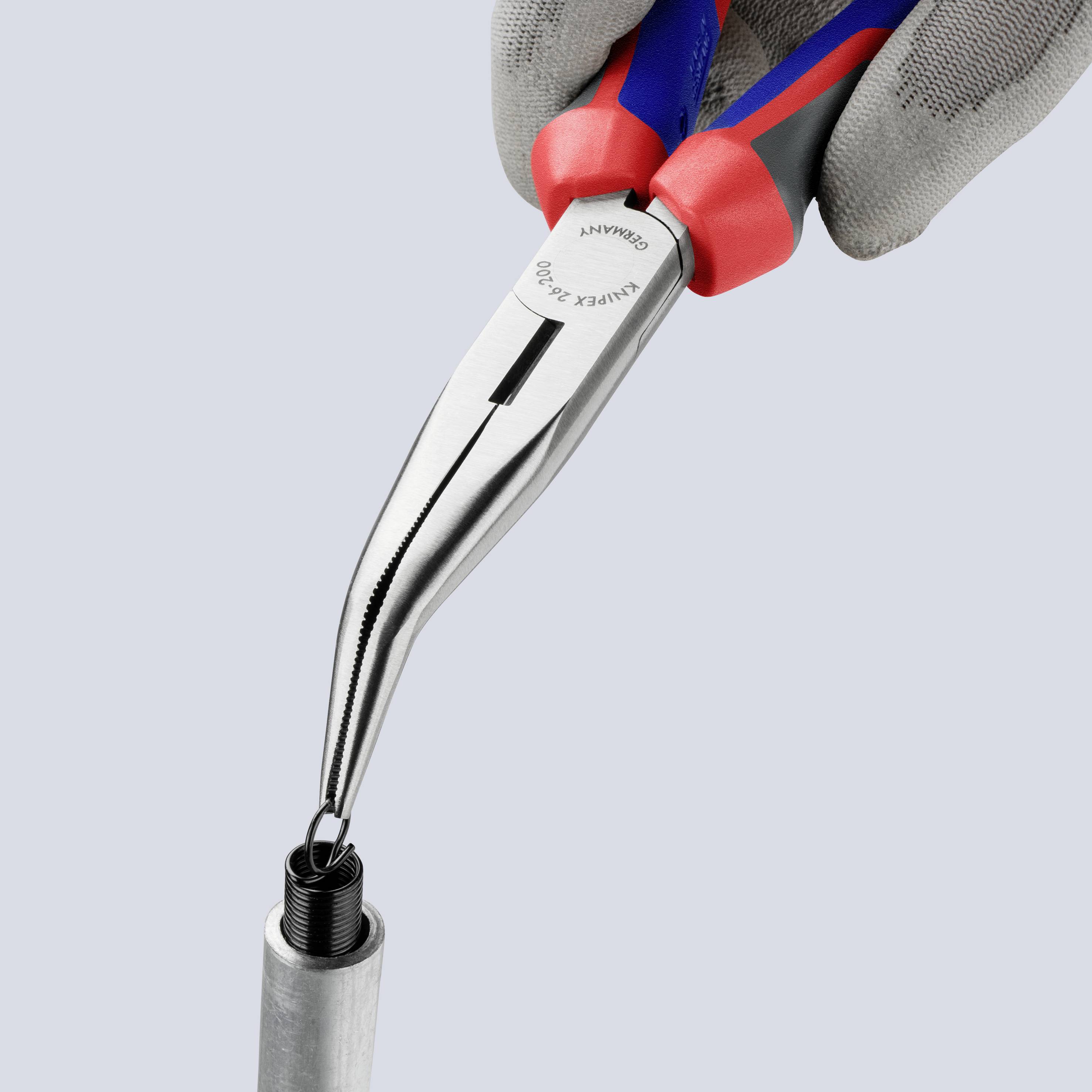 Eine Hand hält eine lange Spitzzange über einem Metallrohr und versucht, ein Objekt herauszuziehen.