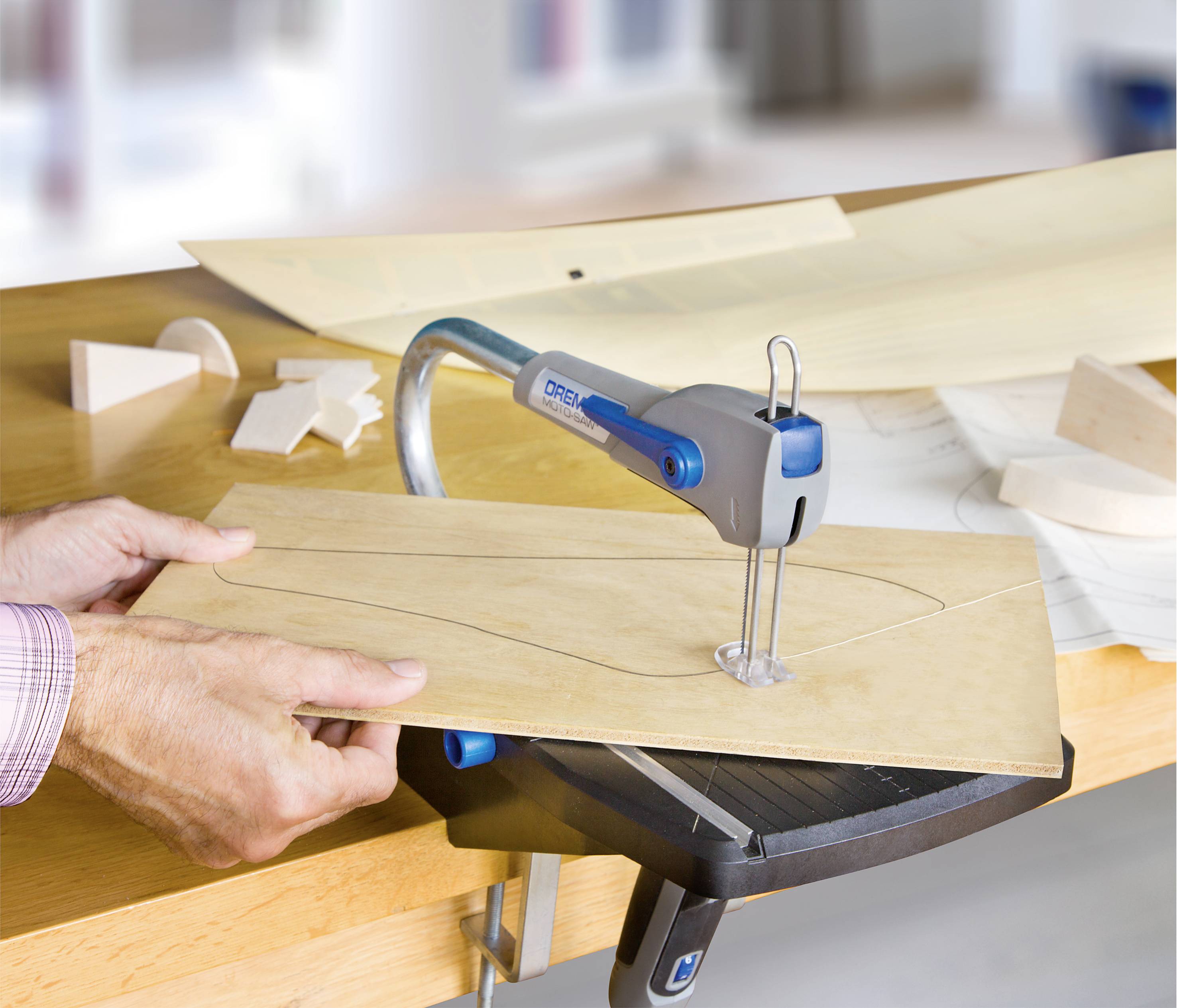 Person benutzt eine Laubsäge, um in einem dünnen Holzbrett eine Form auszuschneiden. Auf dem Tisch liegen weitere Holzteile.