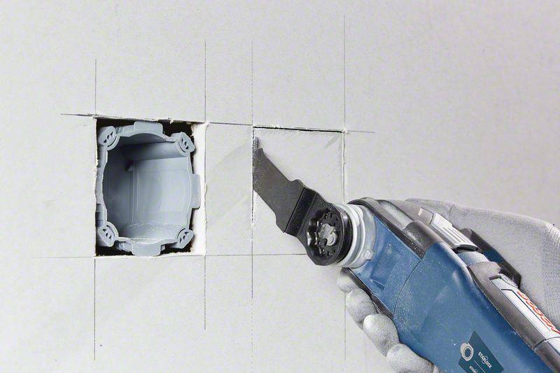 Eine rechteckige Öffnung wird präzise in eine weiße Wand geschnitten, mithilfe eines oszillierenden Multitools mit Sägeblatt.