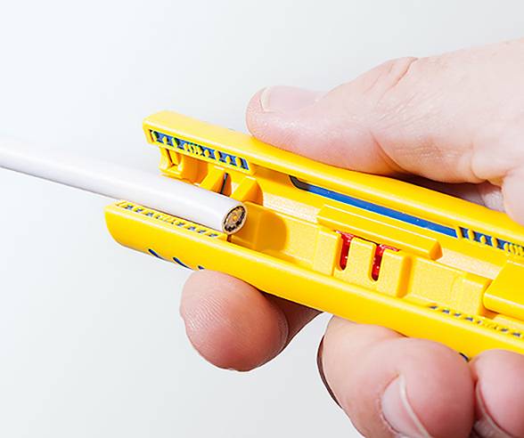 Eine Hand verwendet einen gelben Kabelabisolierer, um die Isolierung von einem weißen Kabel zu entfernen.