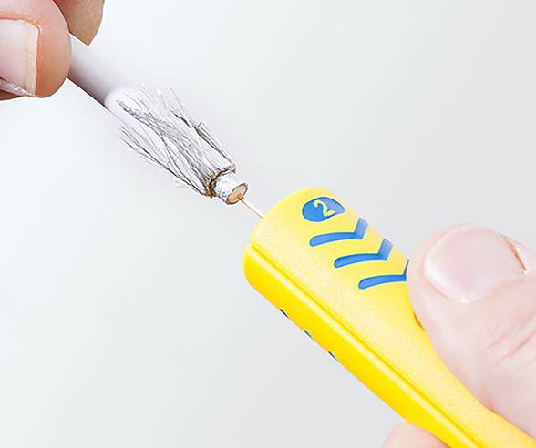 Eine Person, die mit einem gelben Kabelabisolierungswerkzeug Drähte von einem weißen Kabel freilegt, wobei Metallstränge und ein zentraler Kupferdraht sichtbar sind.