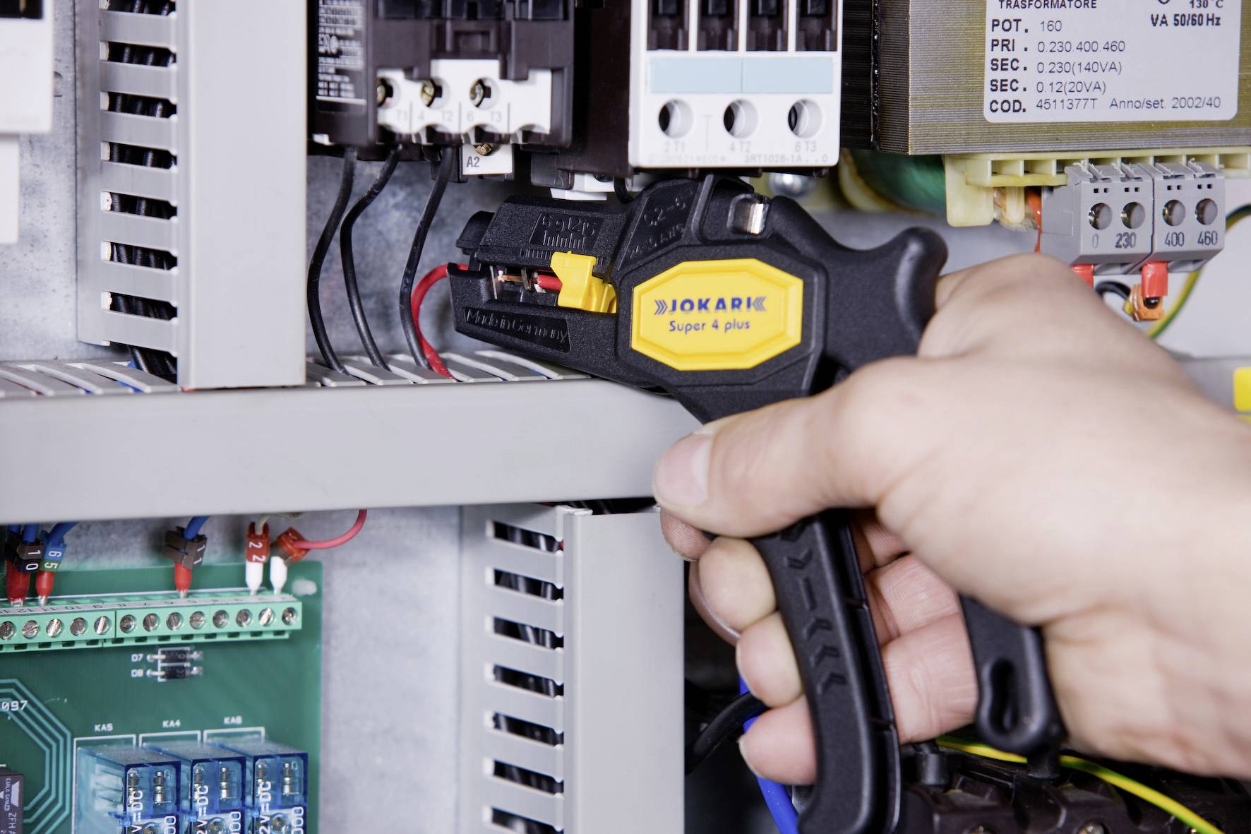 Hand bedient einen Kabelentmanteler, um Kabel im Inneren eines elektrischen Schaltschrankes zu bearbeiten.