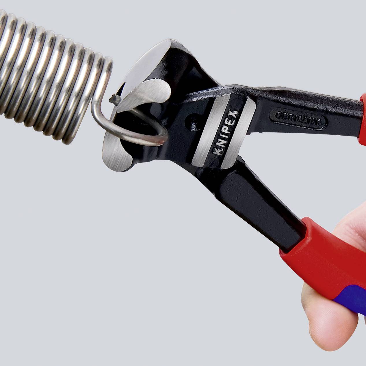 Hand hält eine Knipex-Zange, die einen Metallfederdraht schneidet.