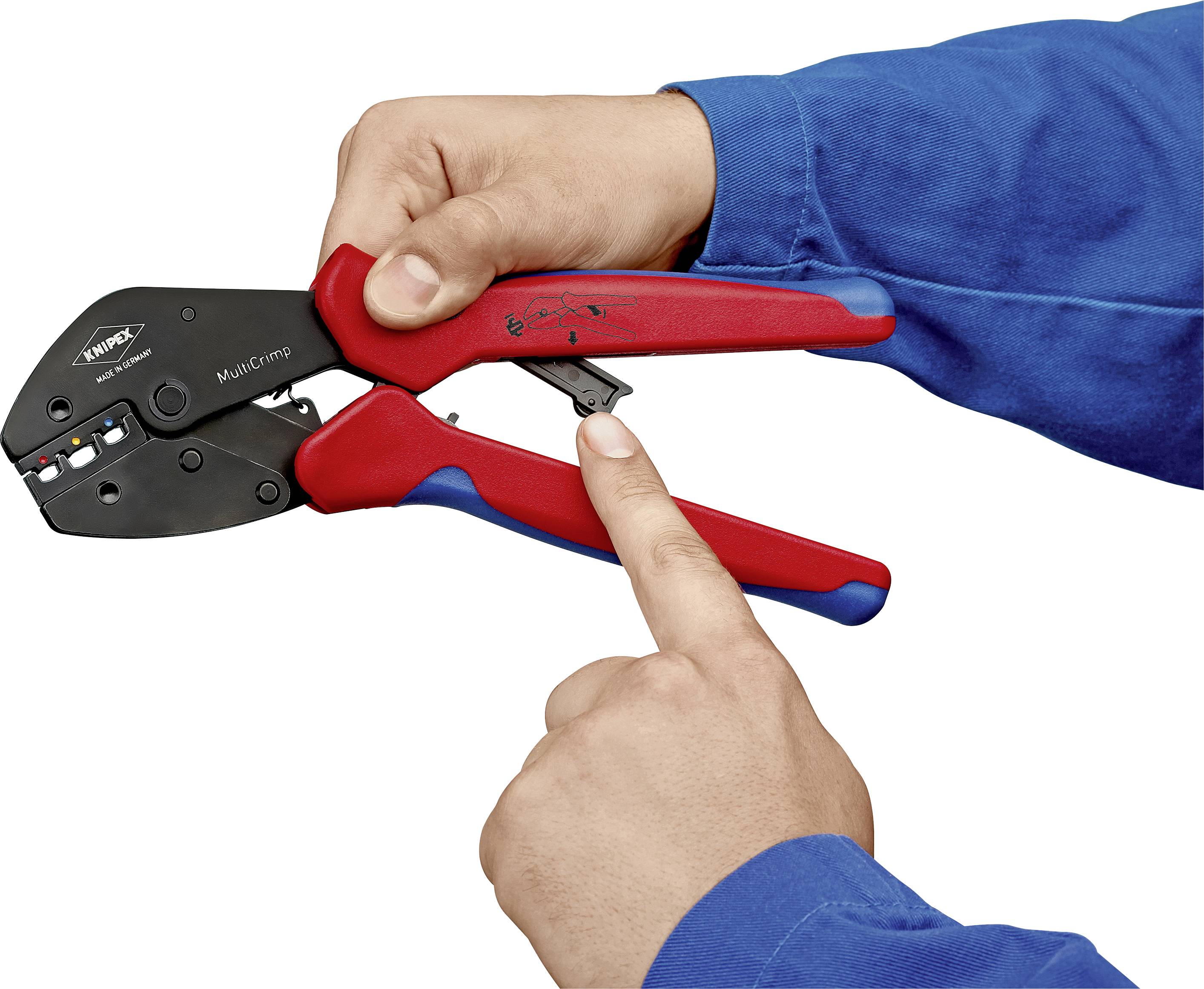 Zwei Hände halten eine rote und schwarze Crimpzange. Eine Hand zeigt auf einen Hebel an der Zange. Die Person trägt einen blauen Pullover.