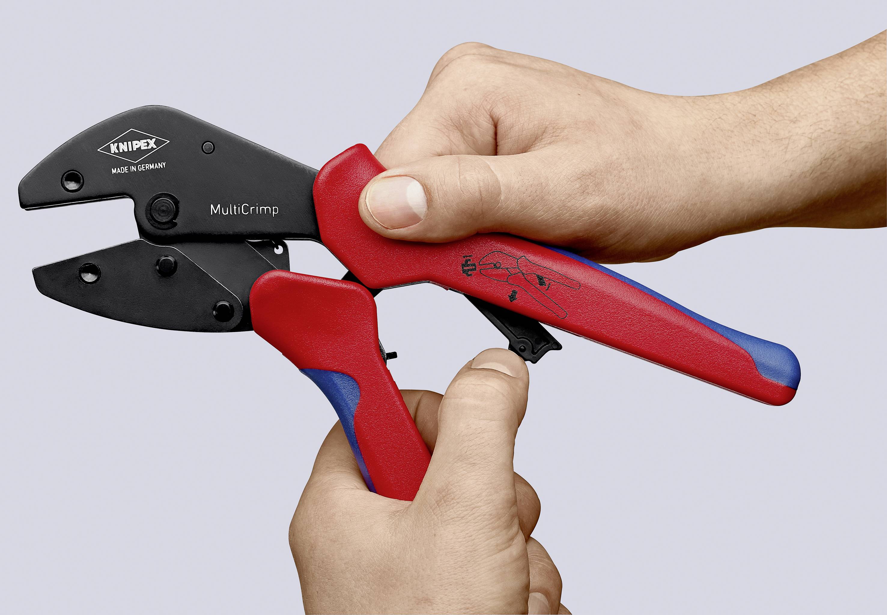 Eine Hand hält eine rote und schwarze Crimpzange der Marke 'KNIPEX', Modell 'MultiCrimp'.