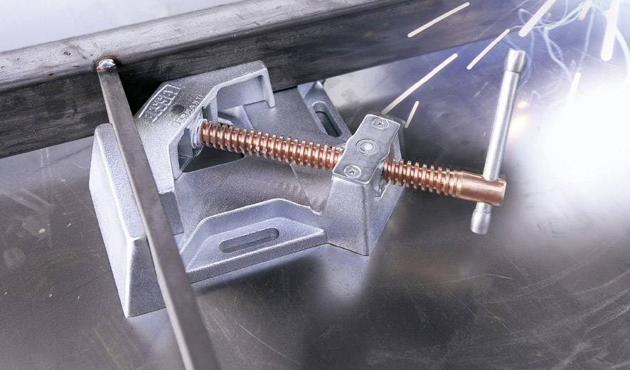 Ein Schraubstock hält ein Metallstück, während Funken von einem Schweißvorgang sprühen. Der Fokus liegt auf der Maschinensicherung.