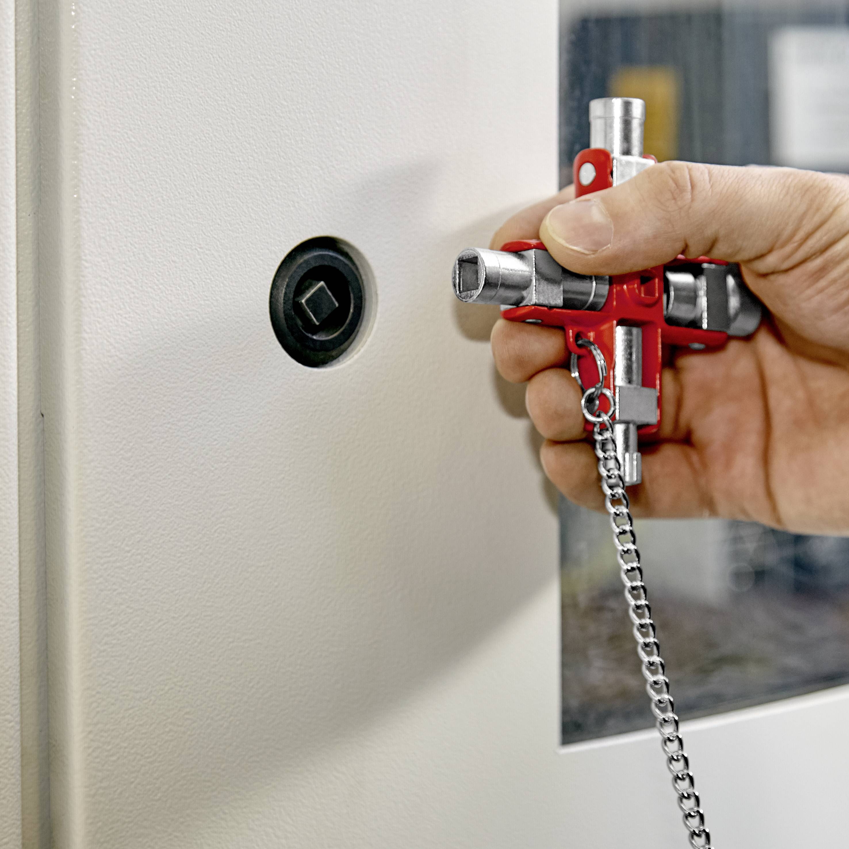 Person benutzt eine rote Schlüsselarmatur zum Öffnen eines Verschlusses an einer metallischen Oberfläche.