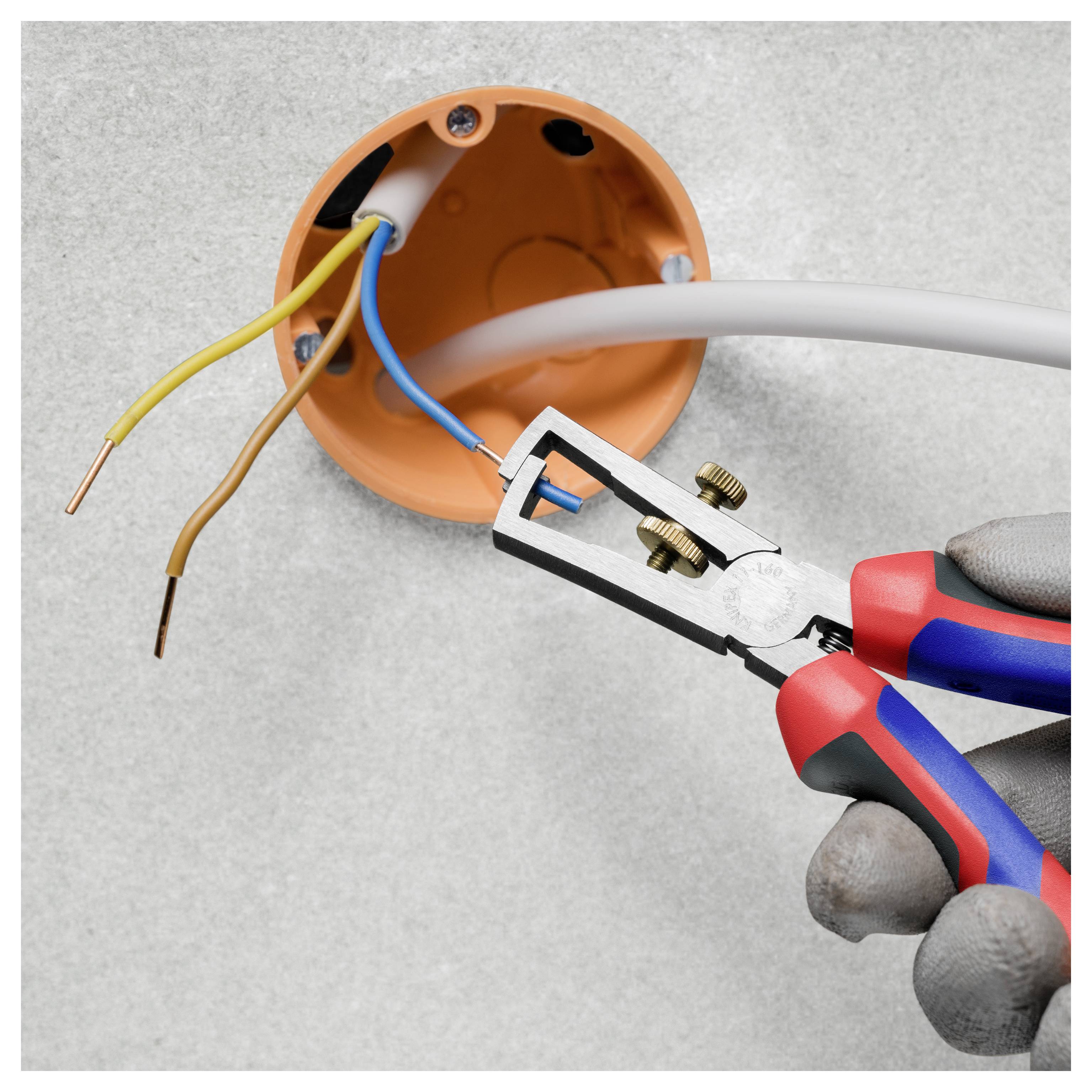 Behandschuhte Hände verwenden eine Zange, um einen blauen Draht von einer runden orangefarbenen Abzweigdose mit freiliegenden elektrischen Drähten zu isolieren.