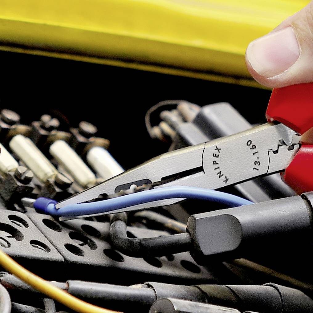Eine rote Zange knipst ein blaues Kabel ab. Im Hintergrund sind elektronische Bauteile zu sehen.