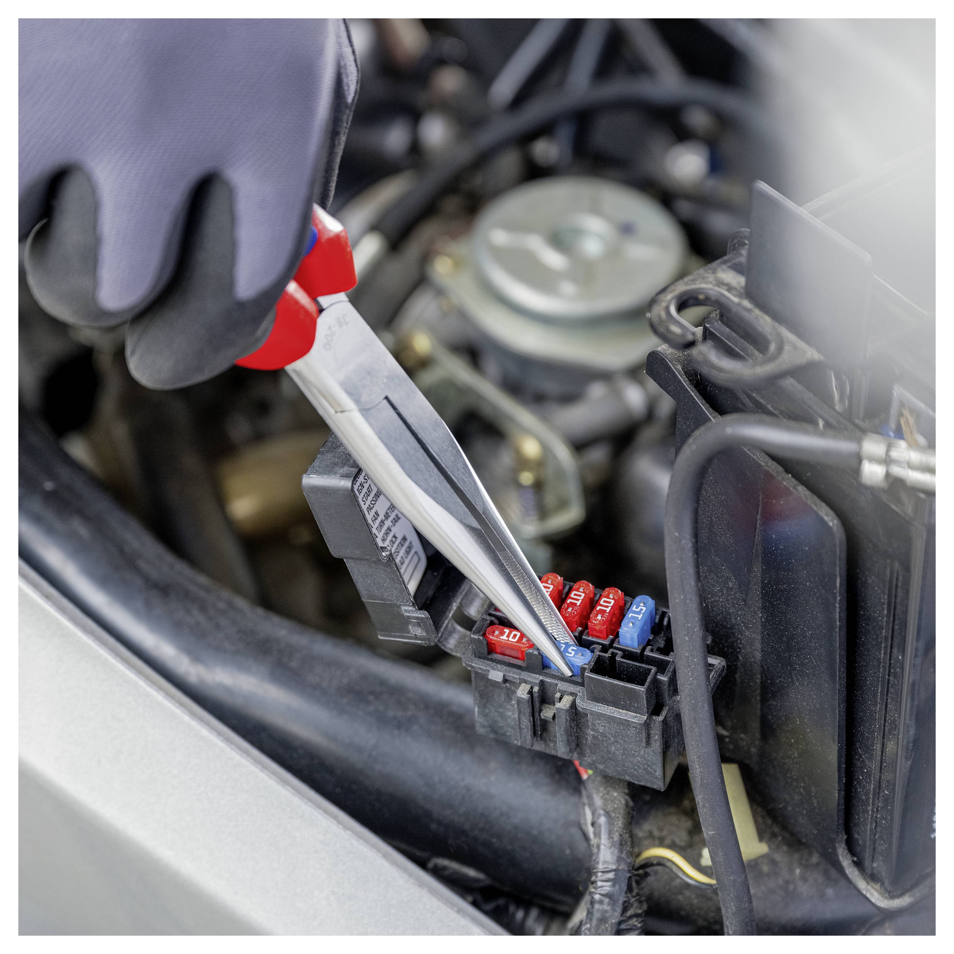 Behandschuhte Hand verwendet eine Testsonde an einer Autosicherungsbox im Motorraum.