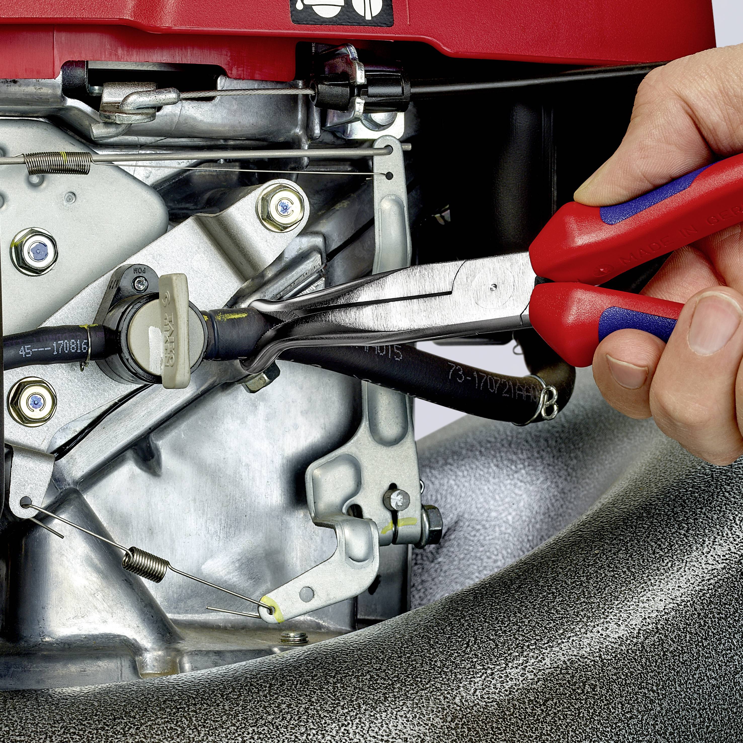 Eine Hand hält eine Zange und justiert die Kabel eines Rasenmähermotors. Mechanische Teile des Motors sind zu sehen.