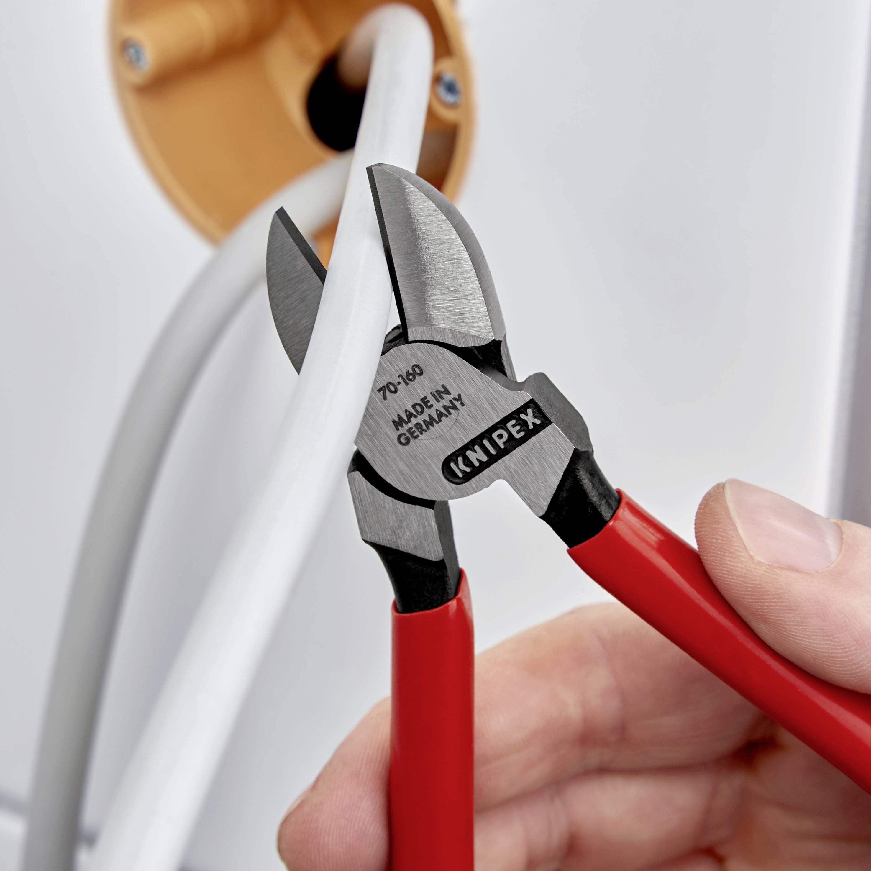 Hand hält eine rote Kabelschere, die ein dickes graues Kabel durchschneidet. Schere ist mit 'Knipex' und 'Made in Germany' beschriftet.