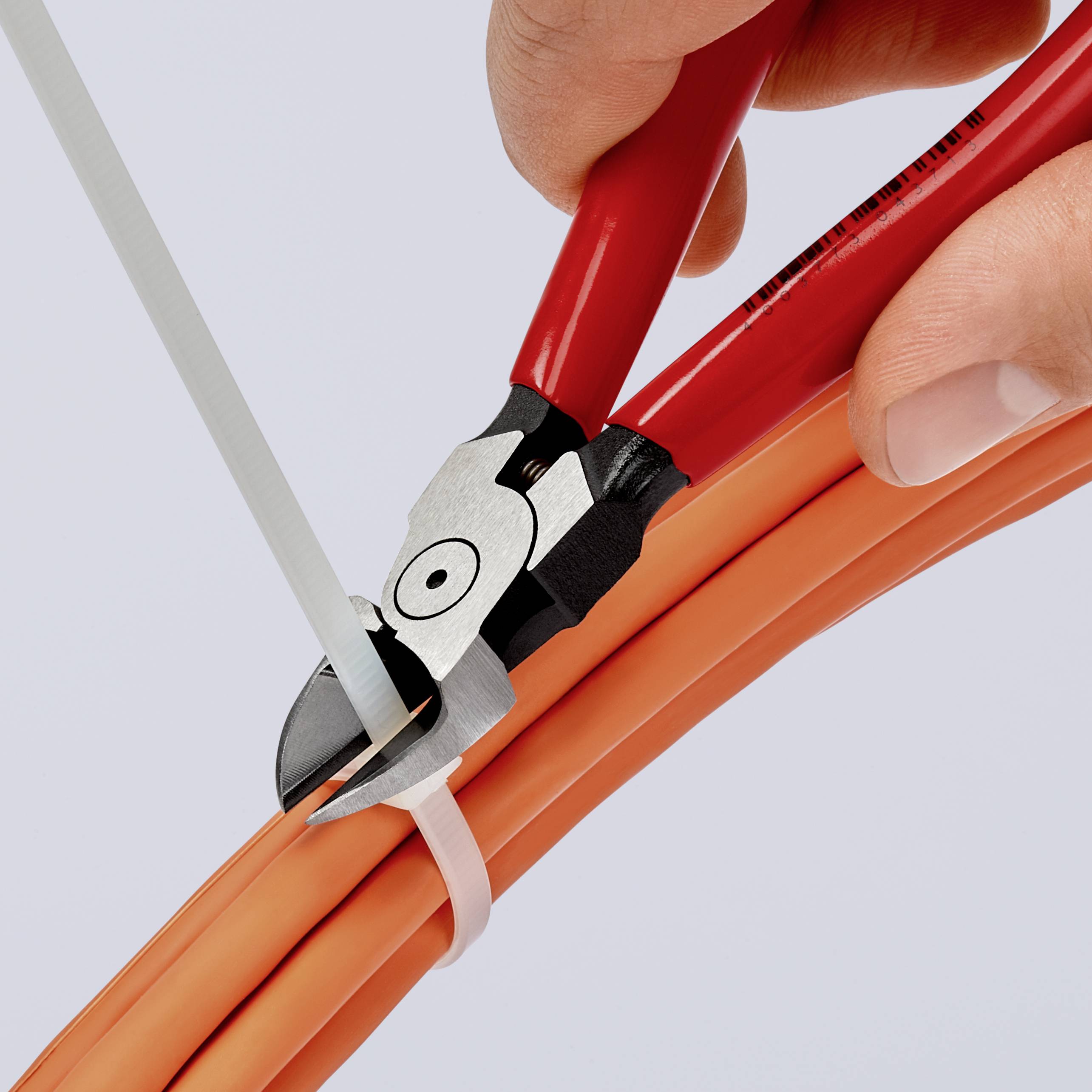 Eine Hand hält einen Seitenschneider und schneidet ein weißes Kabelbindeband, das mehrere orange Kabel zusammenhält.
