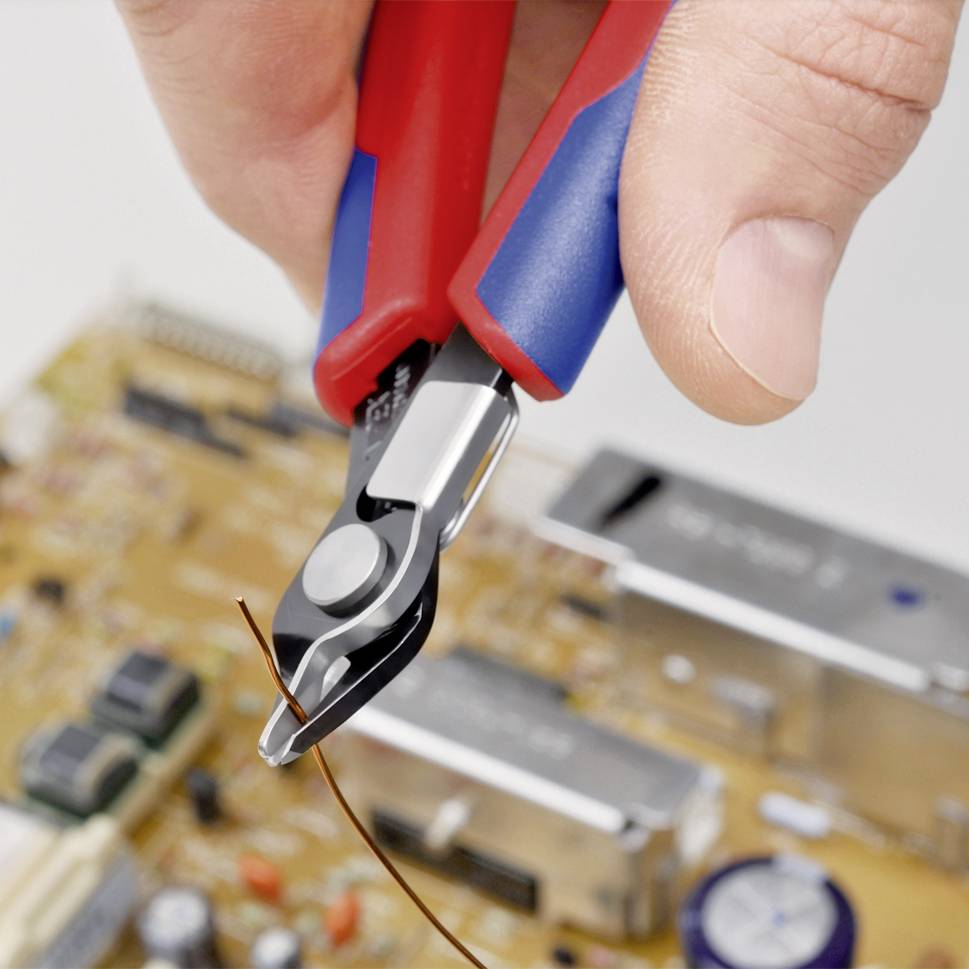 Eine Hand hält einen Seitenschneider, der ein dünnes Kabel über einer elektronischen Platine durchschneidet.