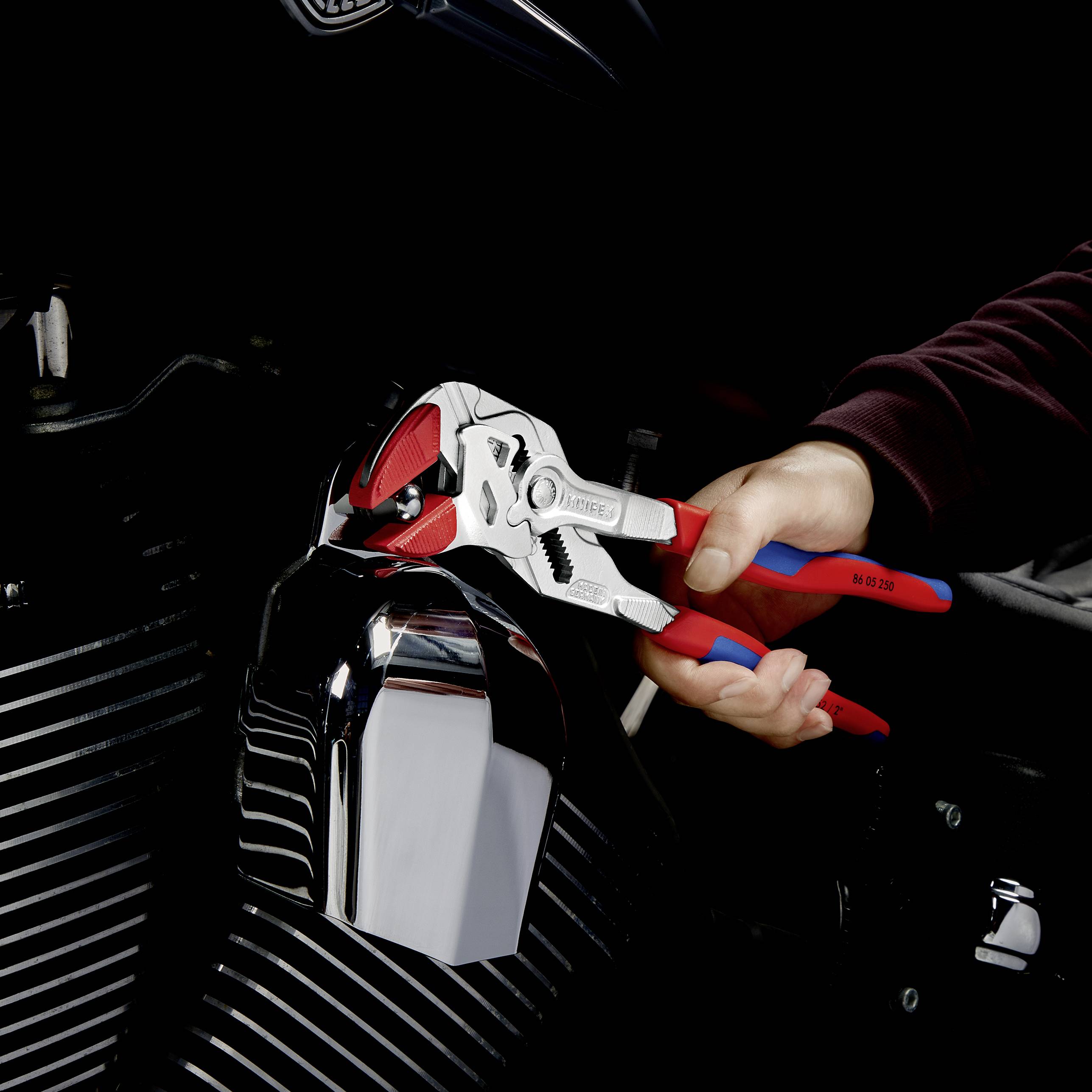 Eine Hand hält eine verstellbare Zange, während sie an einem Motorradmotor arbeitet. Die Zange ist geöffnet und greift um eine Metalloberfläche.