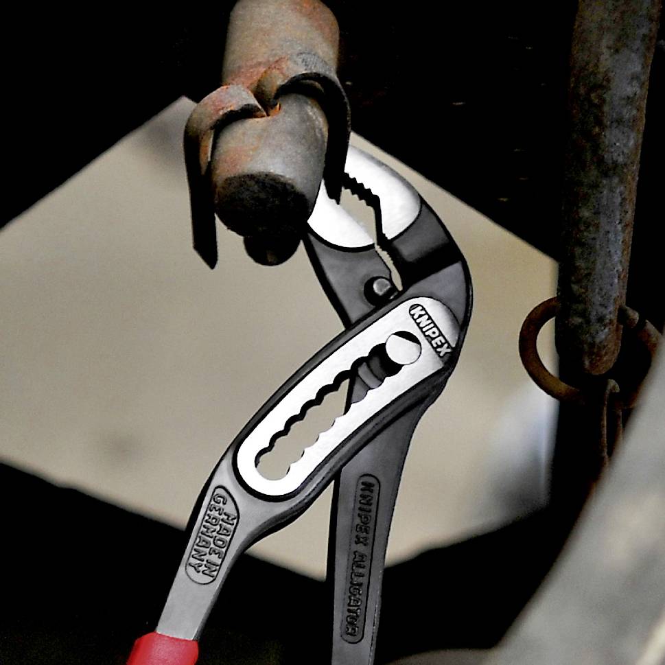 Zange greift um eine Metallschraube, zeigt festziehende Aktion in einer Werkstattumgebung mit Fokus auf das Werkzeug.