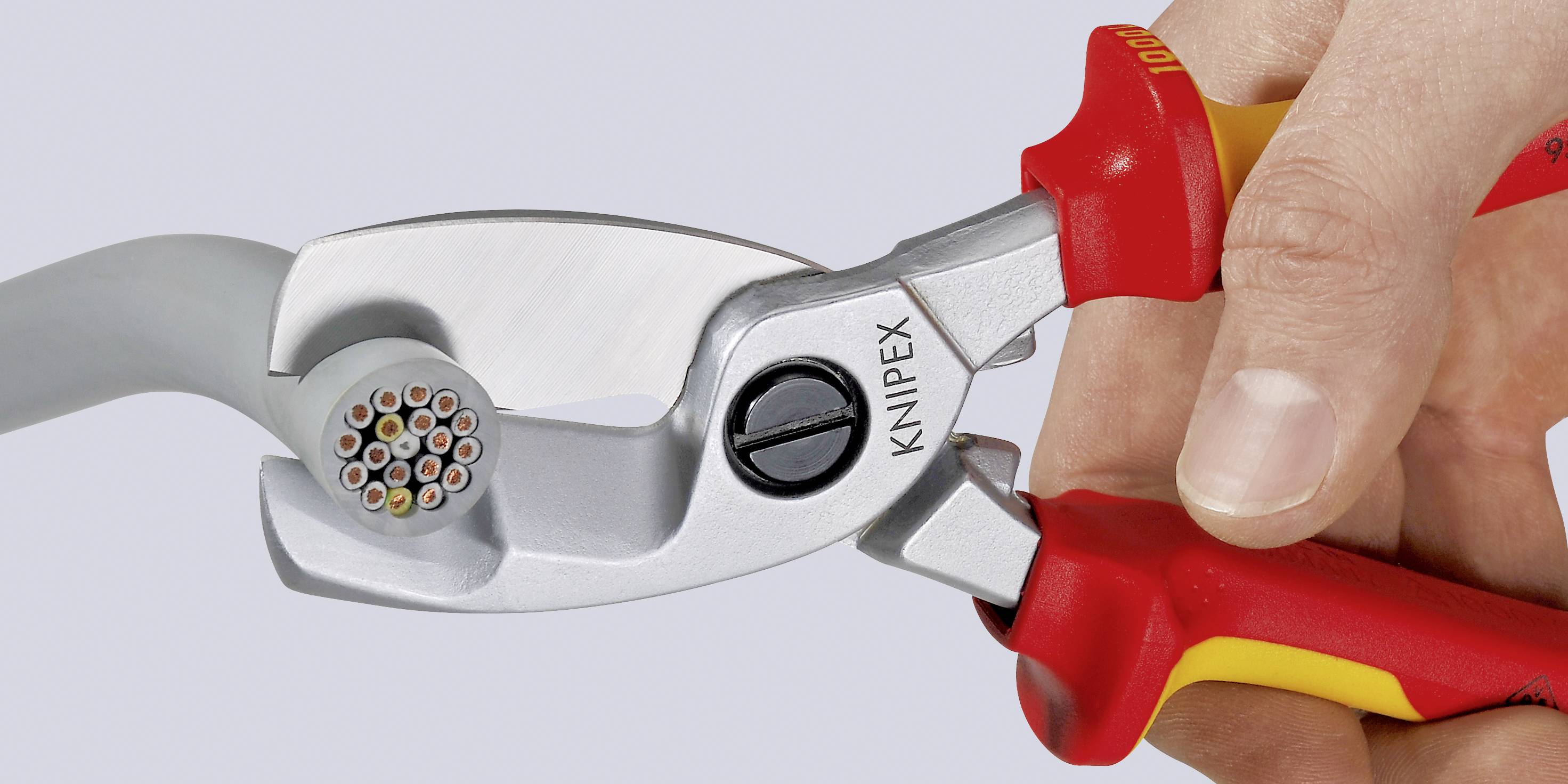 'KNIPEX'-Kabelschneider schneidet ein dickes, rundes Kabel. Gehalten von einer Hand. Werkzeug ist silbern mit roten Griffen.