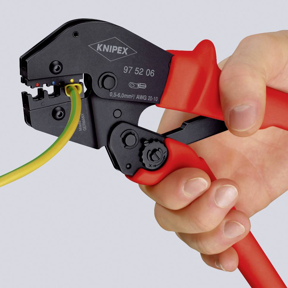 Eine Hand hält eine rote Crimpzange der Marke Knipex, die ein grün-gelbes Kabel durchtrennt.