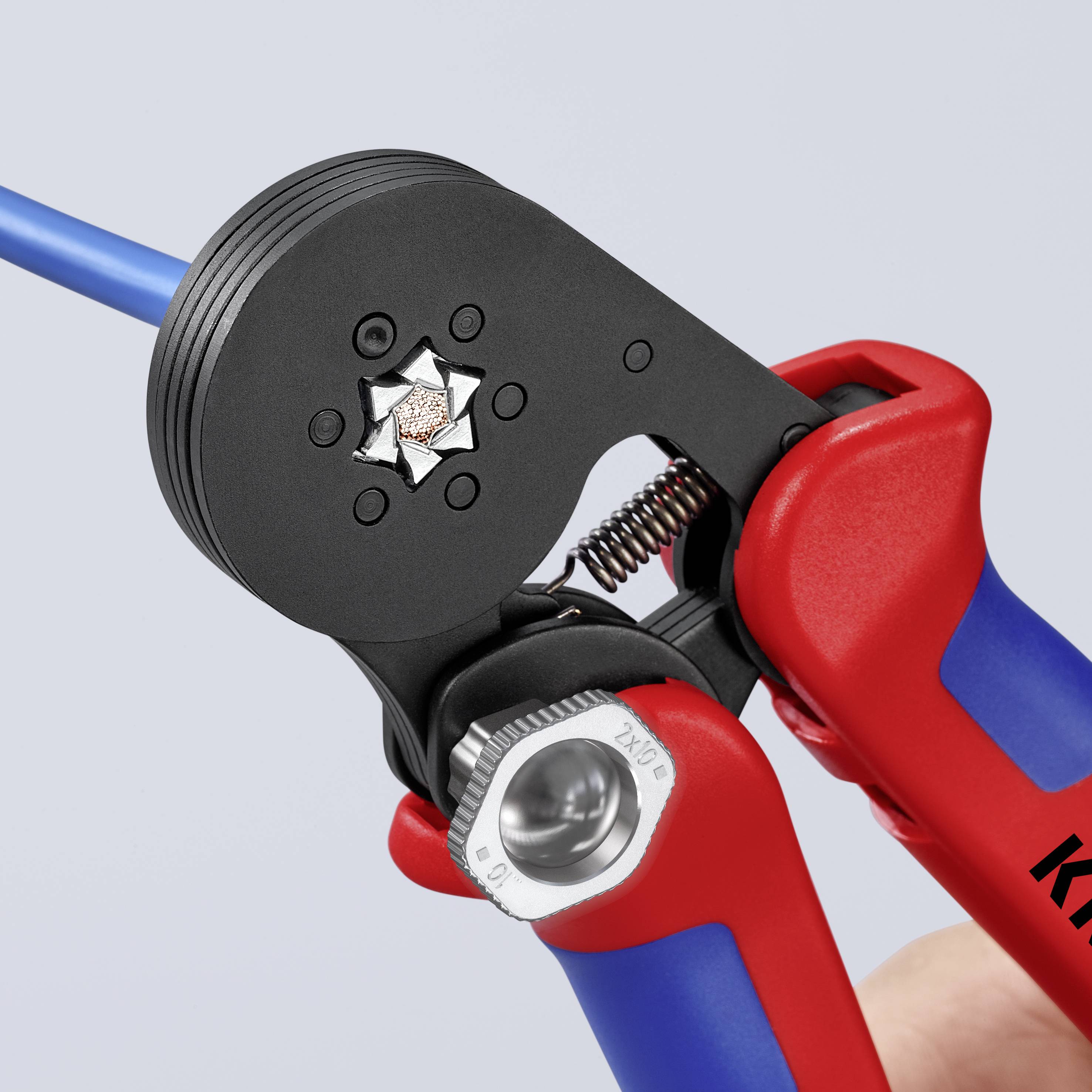 Eine rote Crimpzange hält ein blaues Kabel. Die Zange befindet sich in Nahaufnahme und zeigt den Crimpmechanismus detailliert.