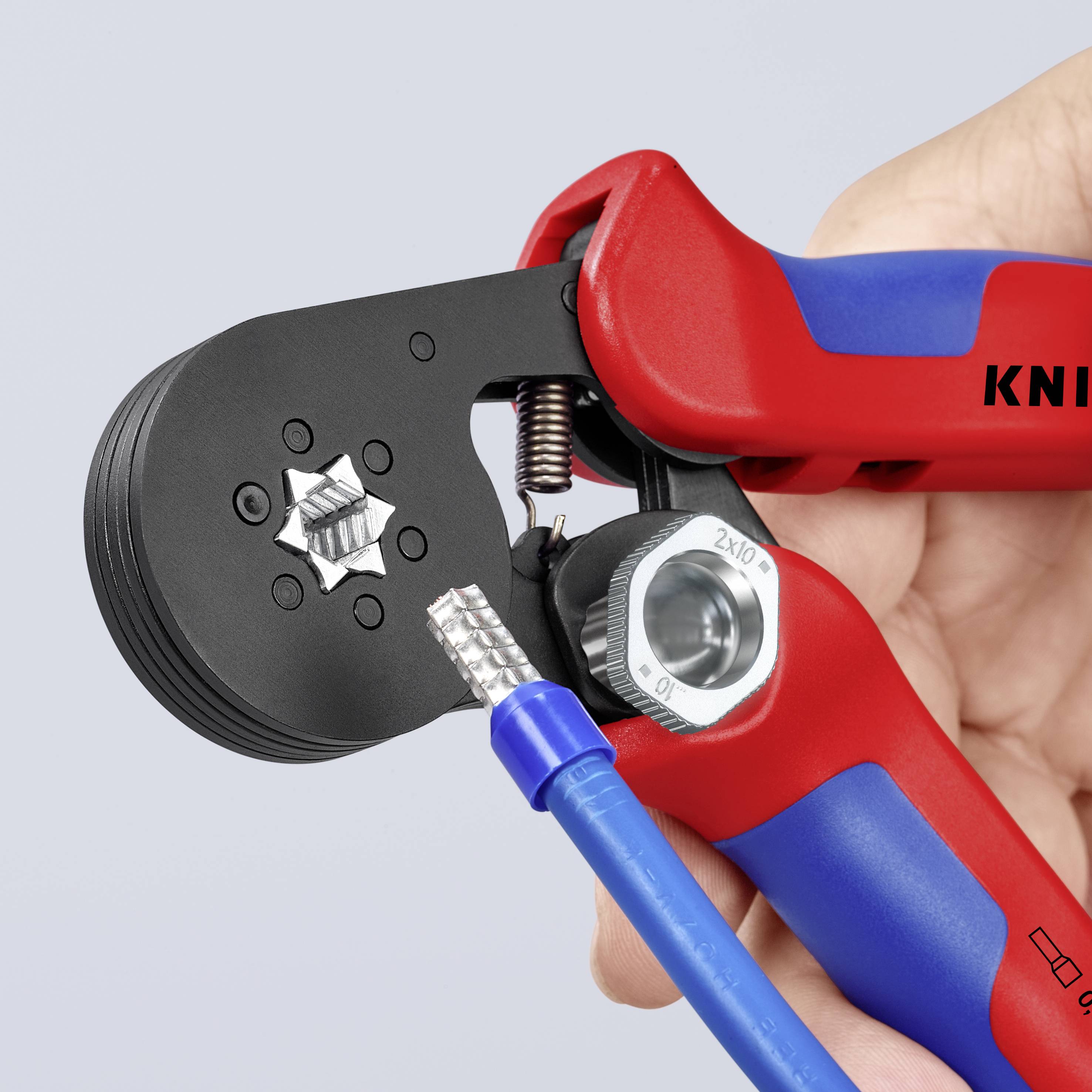 Person hält eine Crimpzange, die dabei ist, ein elektrisches Kabel zu verarbeiten. Werkzeug zeigt Markierung 'KNIP'.