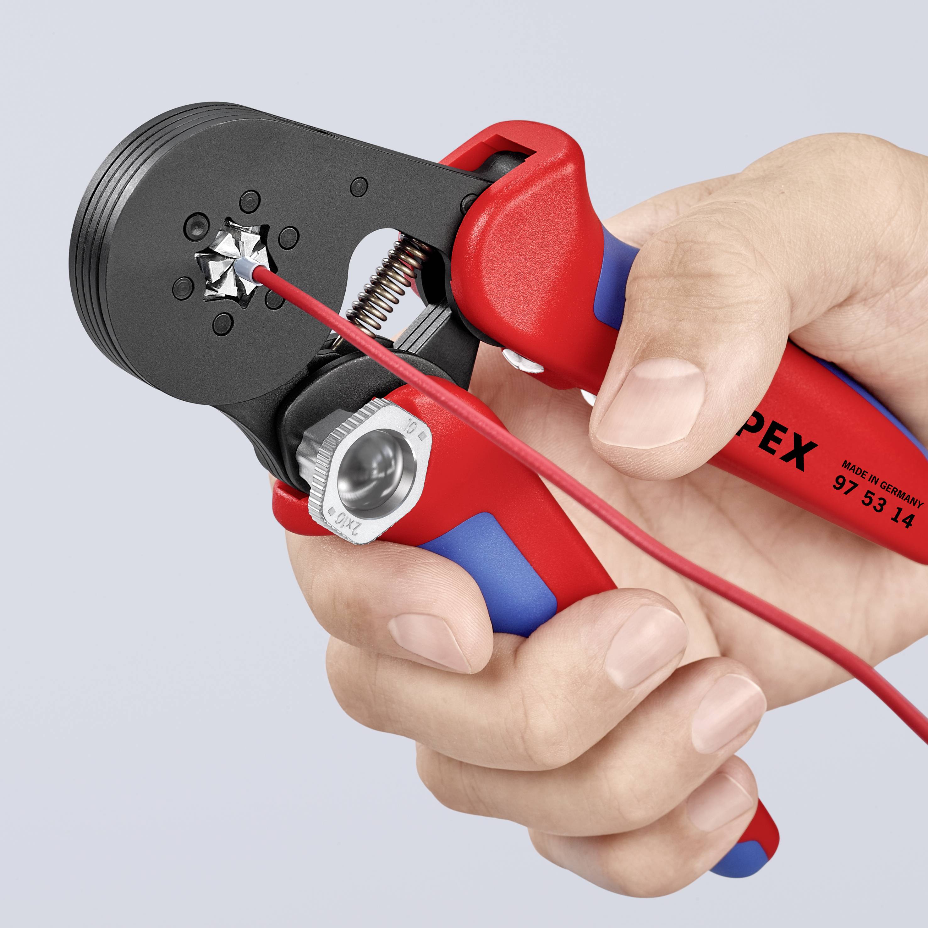Hand hält eine rote und blaue Crimpzange. Ein rotes Kabel wird in die Zange eingeführt, um einen Metallkabelschuh zu crimpen.