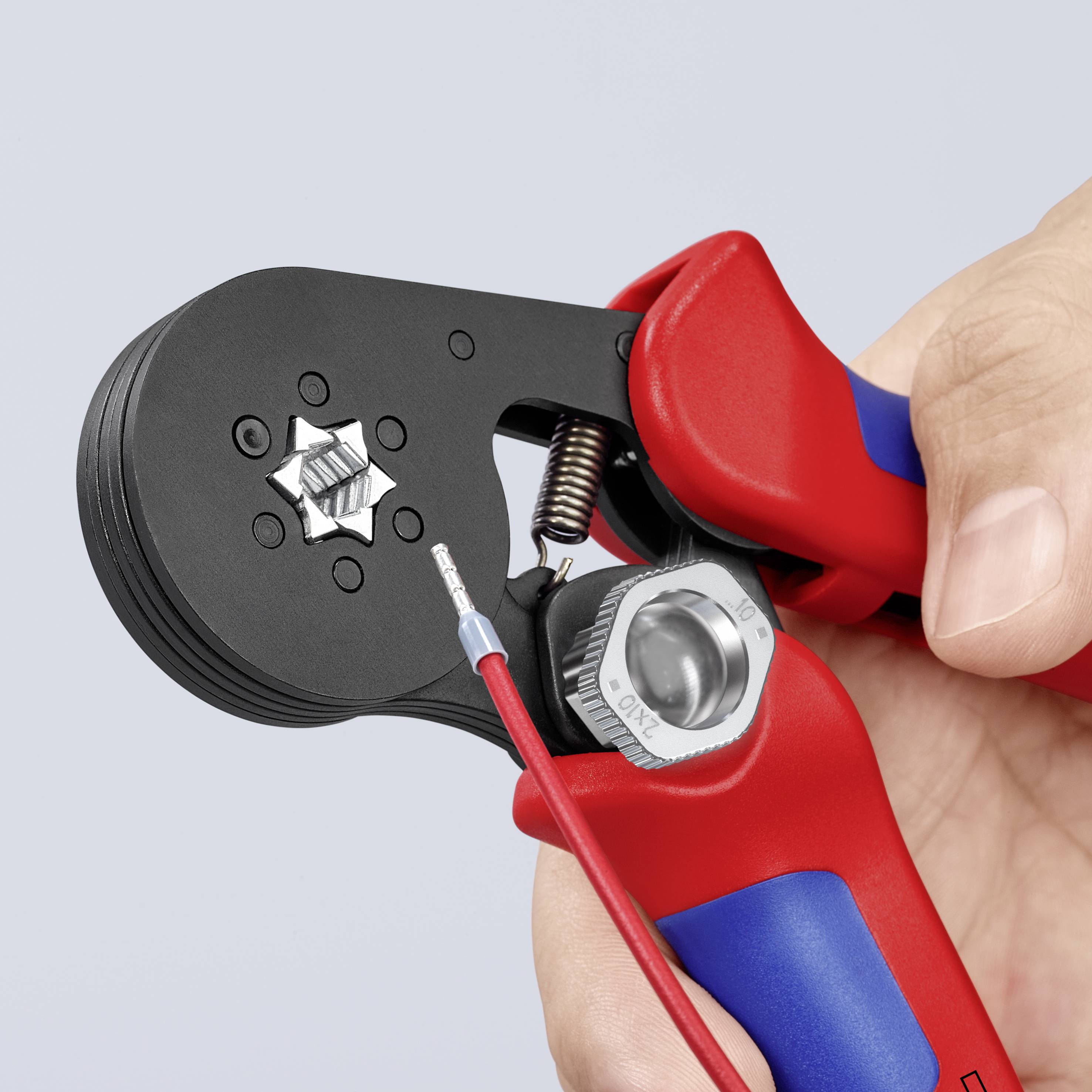 Eine Hand hält eine rote Crimpzange, die einen Draht mit einem Metallstecker bearbeitet.