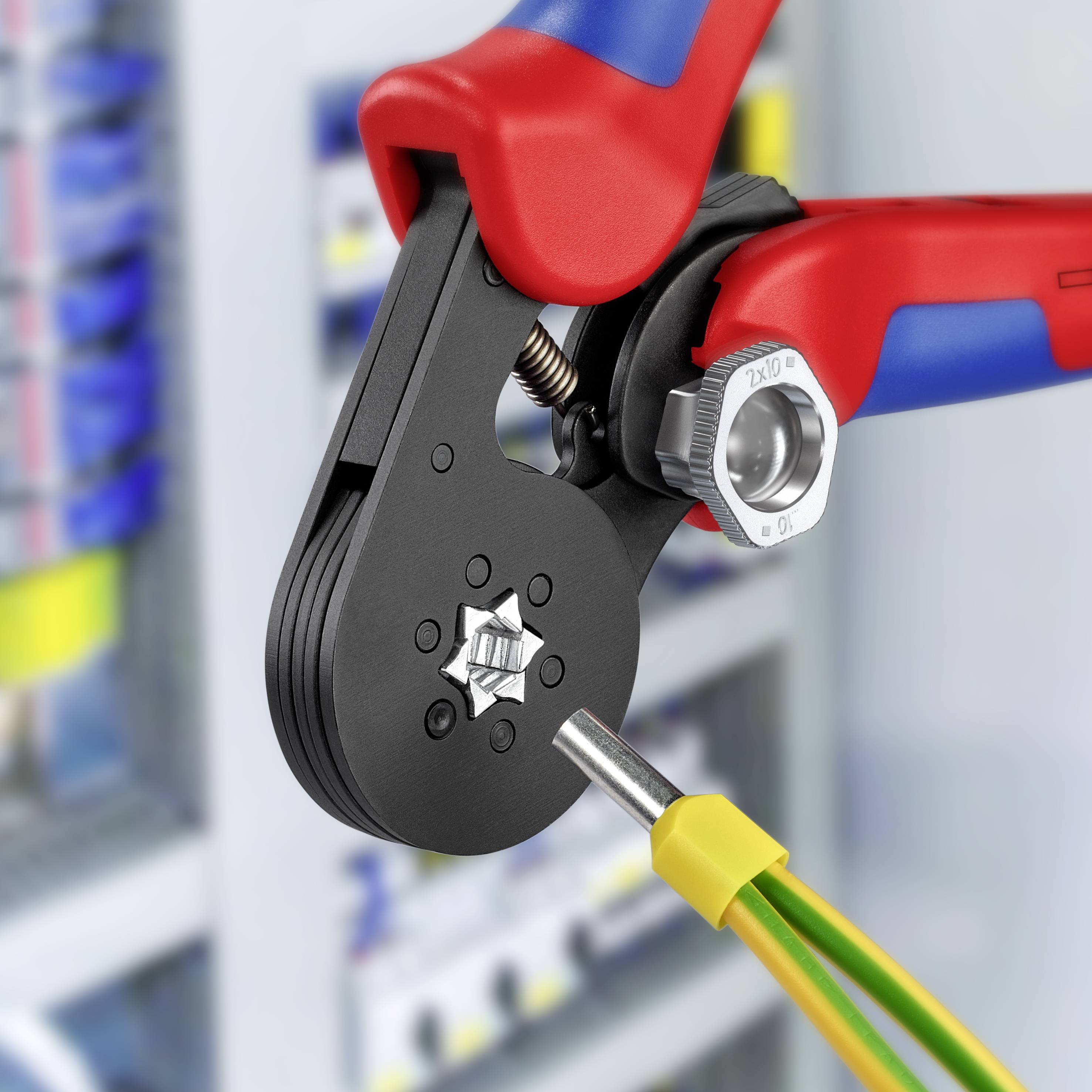 Eine rote und blaue Crimpzange setzt eine gelb-grüne elektrische Aderendhülse in einer Werkstatt fest.