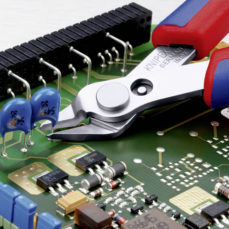 Eine Nahaufnahme einer Platine mit elektronischen Komponenten, darunter blaue Kondensatoren und eine Kombizange, die bereit zum Schneiden ist.