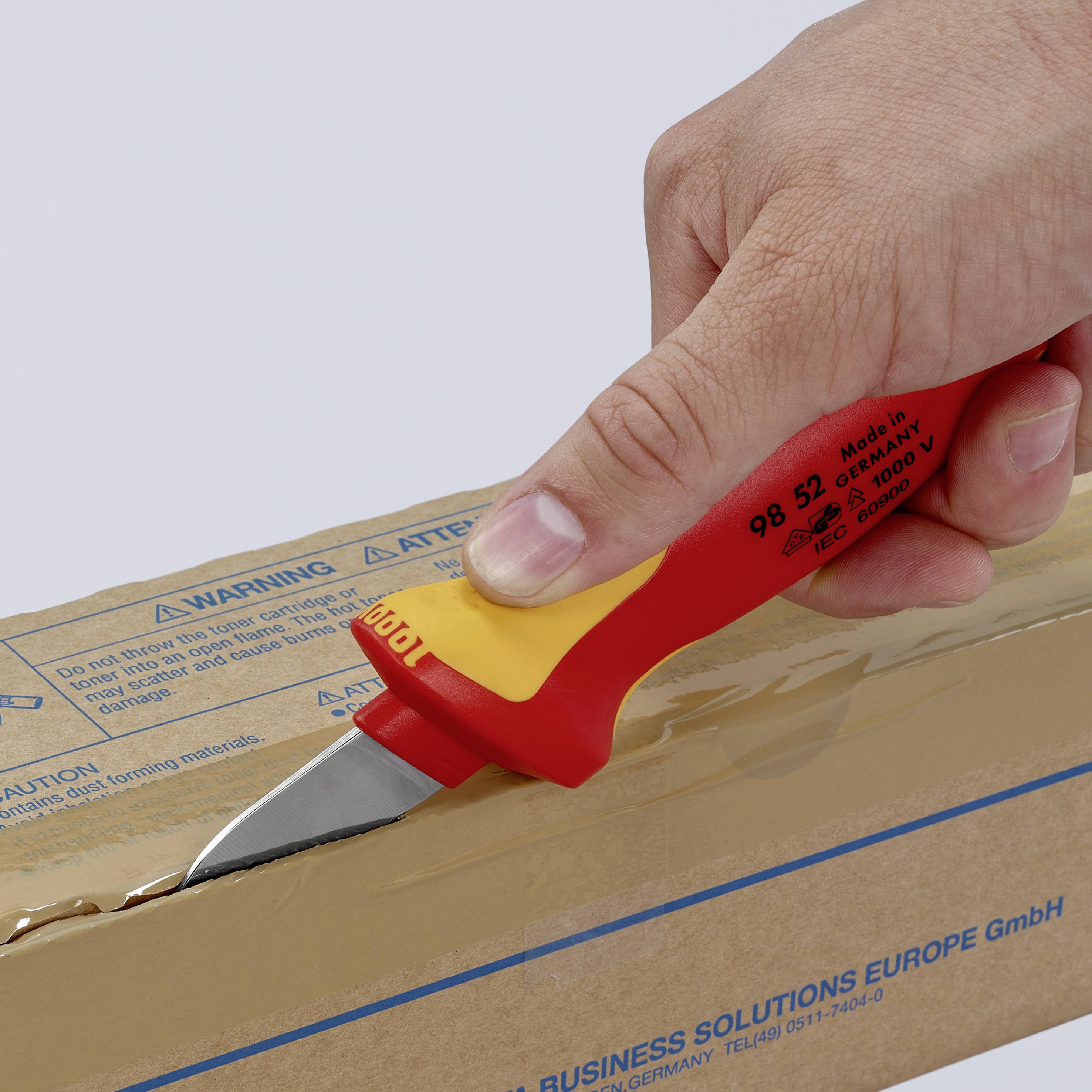 Eine Hand schneidet mit einem gelben Sicherheitsmesser einen Karton auf. Der Karton zeigt den Aufdruck einer Geschäftsadresse unten.