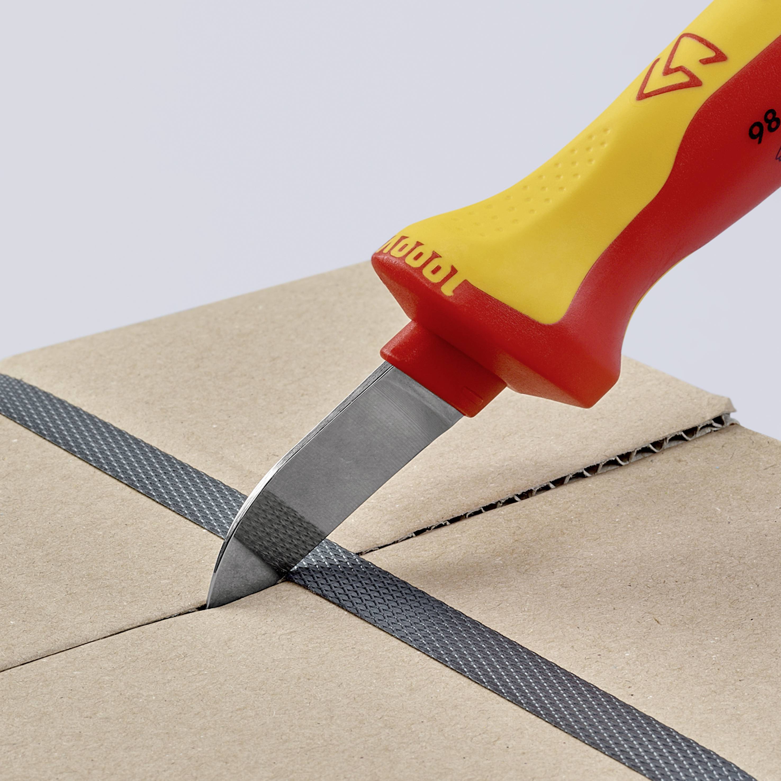 Ein gelbes und rotes Cutter-Messer schneidet durch Karton. Das Messer hat eine kurze, graue Klinge und ergonomischen Griff.
