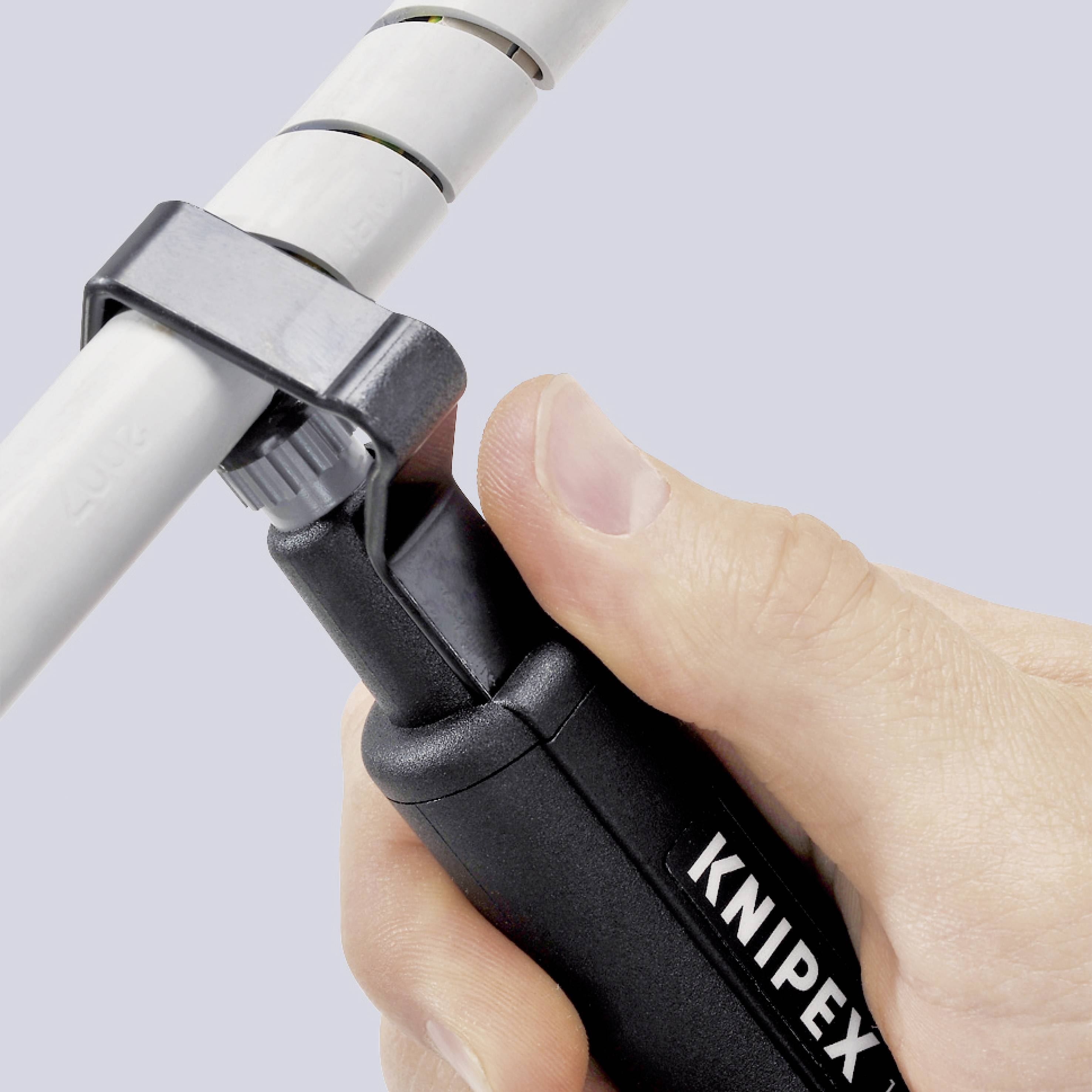 Eine Hand hält ein Rohrschneider-Werkzeug von Knipex. Das Werkzeug schneidet ein weißes Rohr.