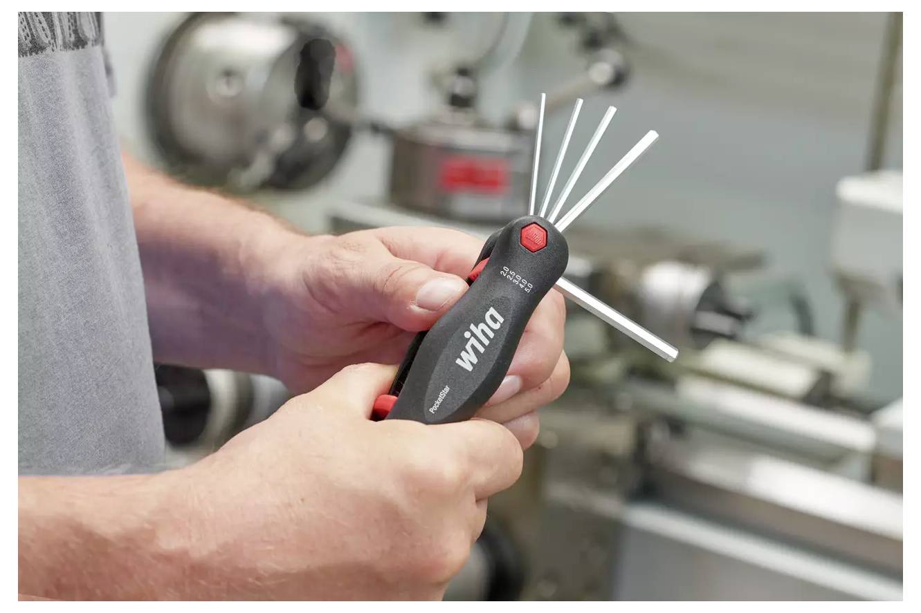 Eine Person, die ein Multitool mit mehreren ausgefahrenen Metallsechskantschlüsseln hält, in einer Werkstattumgebung mit Maschinen im Hintergrund.
