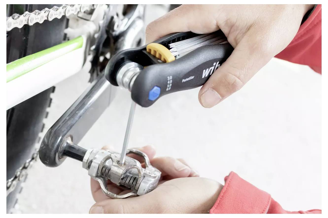 Person, die ein Fahrradpedal mit einem Multitool einstellt.