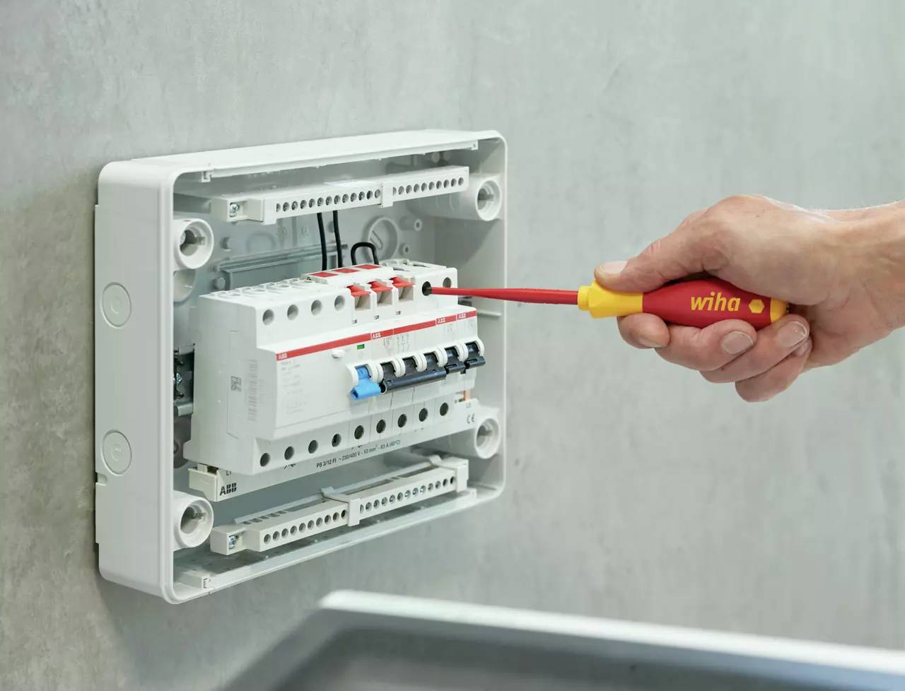 Eine Hand zieht mit einem Schraubendreher den Schalter einer elektrischen Sicherung in einem Schaltkasten an.