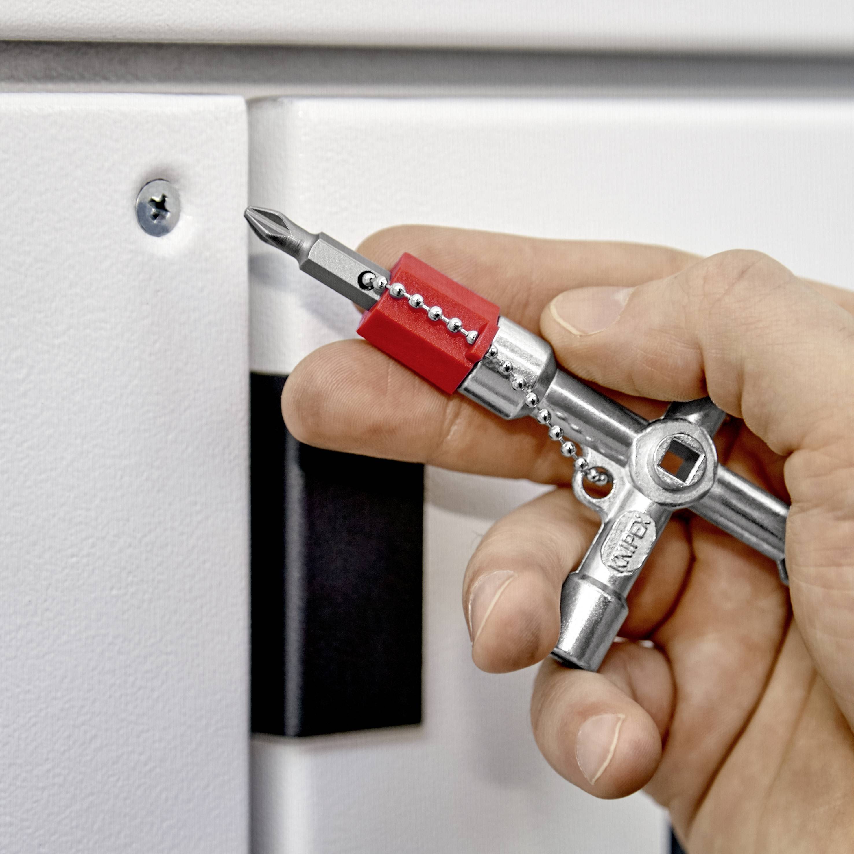 Eine Hand hält einen Kreuzschlüssel mit einem Schraubenzieheraufsatz, der in eine Schraube an einem weißen Gerät eingesetzt wird.