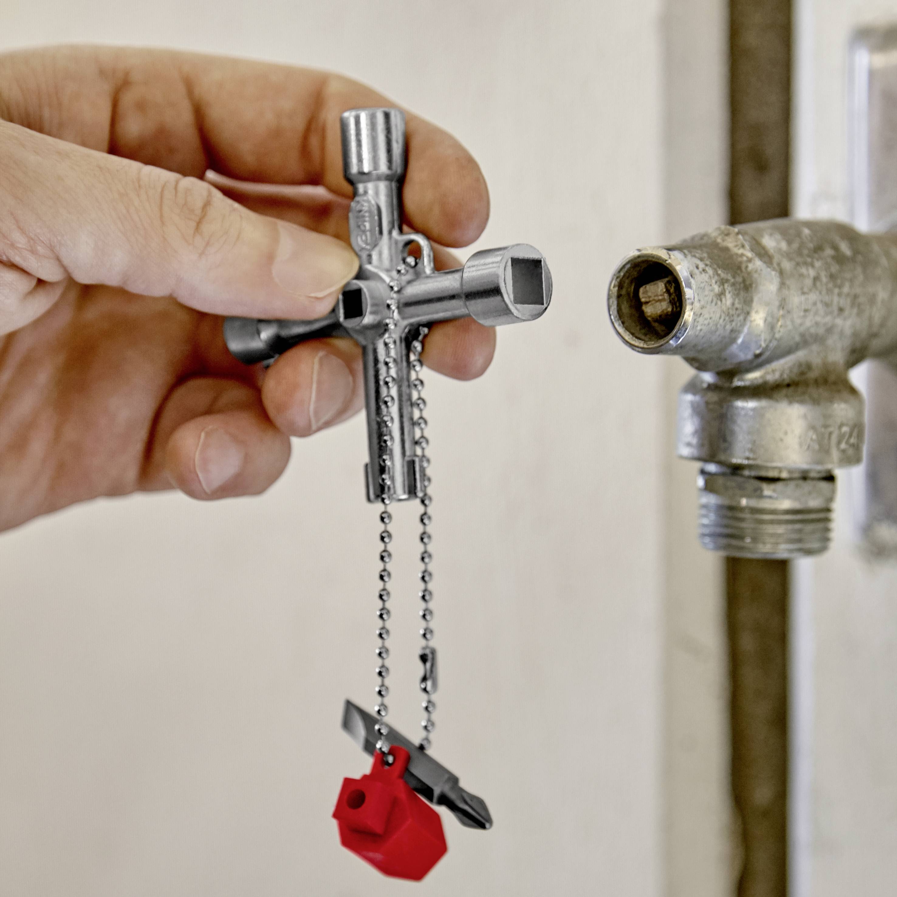 Hand, das einen Wasserhahnkreuzschlüssel hält. Der Schlüssel ist schlüsselförmig und hängt an einer Kette, die an einem Lego-Stein befestigt ist.