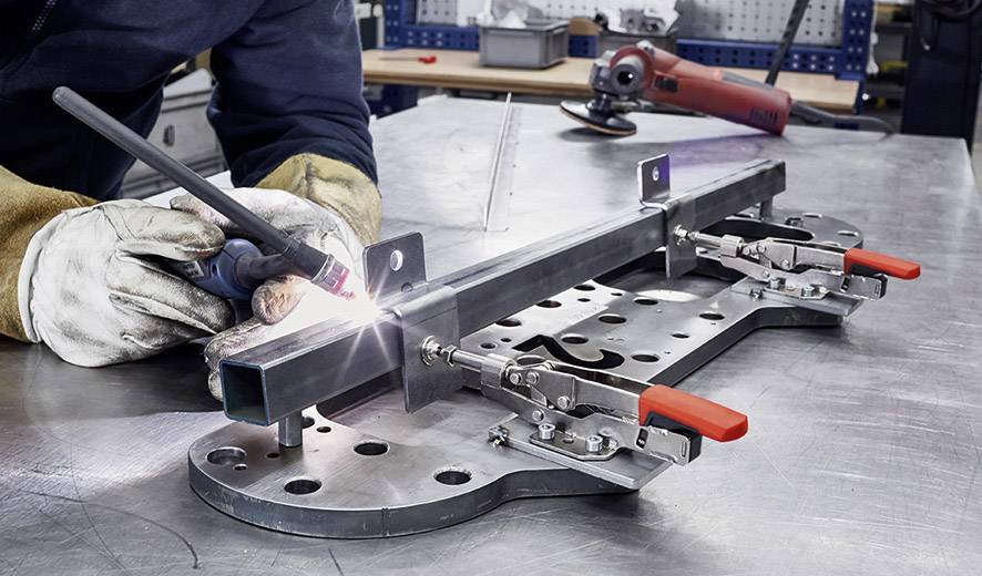 Eine Person schweißt ein Metallstück an einem geordneten Arbeitsplatz in einer Werkstatt.