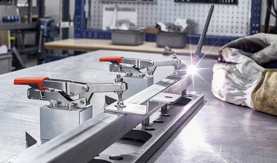 Schweißtisch in einer Werkstatt, auf dem ein Metallstück mit Klemmen befestigt ist. Ein Lichtstrahl zeigt den Schweißvorgang.