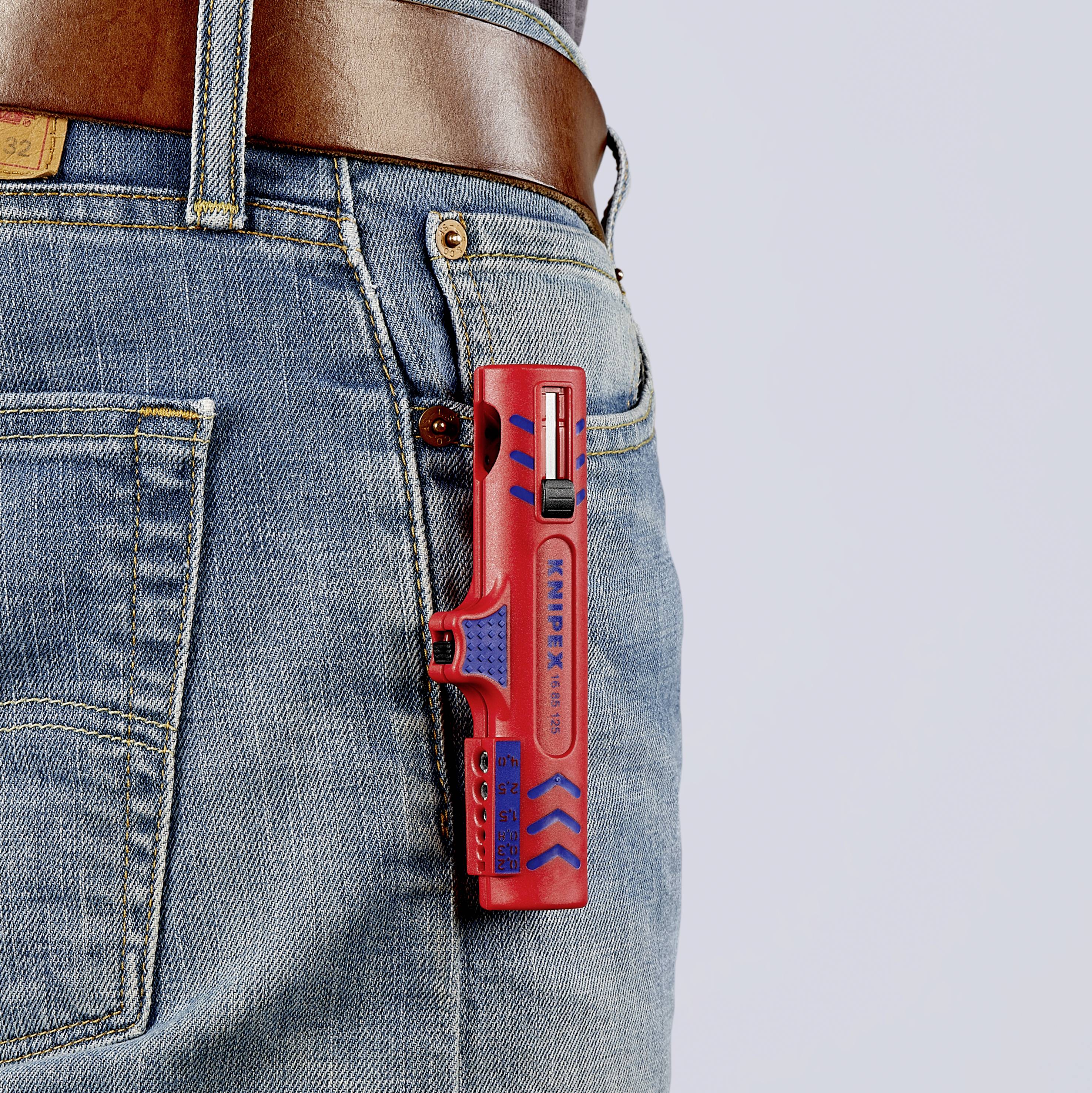 Ein rotes Multitool steckt an der Gesäßtasche einer blauen Jeans, gesichert durch einen braunen Ledergürtel.