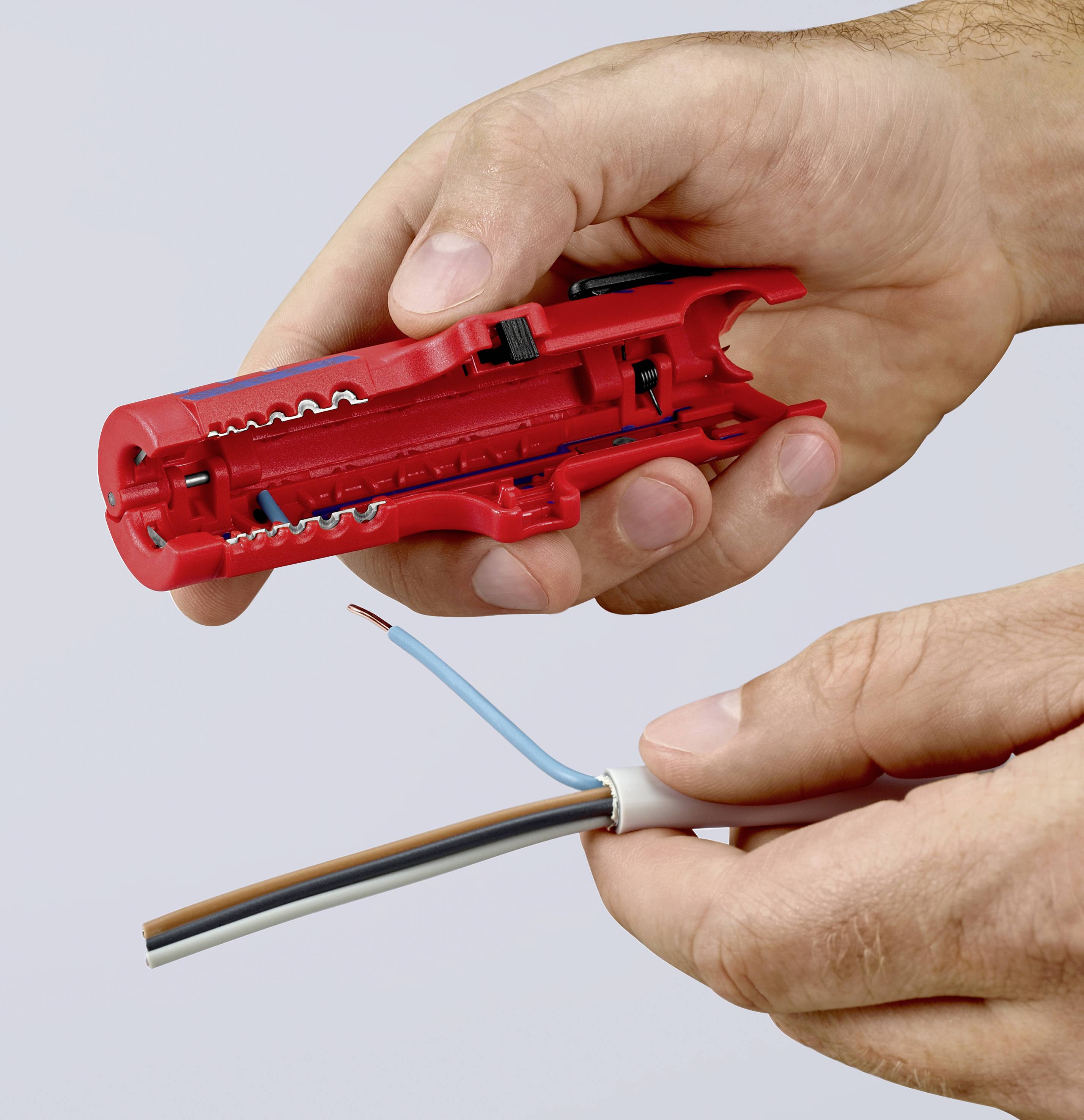 Zwei Hände halten einen roten Abisolierer und ein dreifarbiges Kabel, während das Kabel für den Anschluss vorbereitet wird.