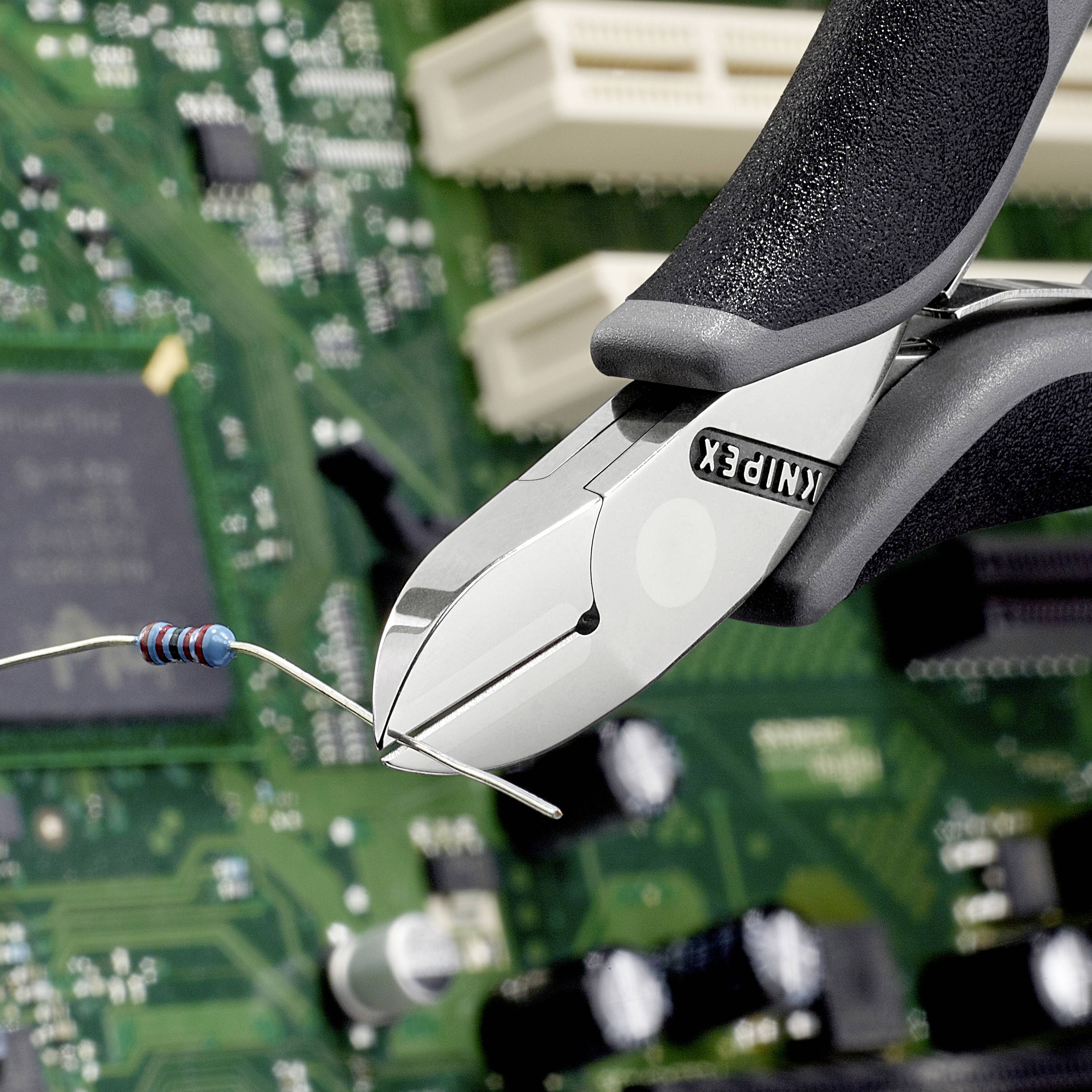 Eine Drahtschneiderzange schneidet einen blauen Widerstand über einer grünen Platine mit sichtbarer Elektronik.