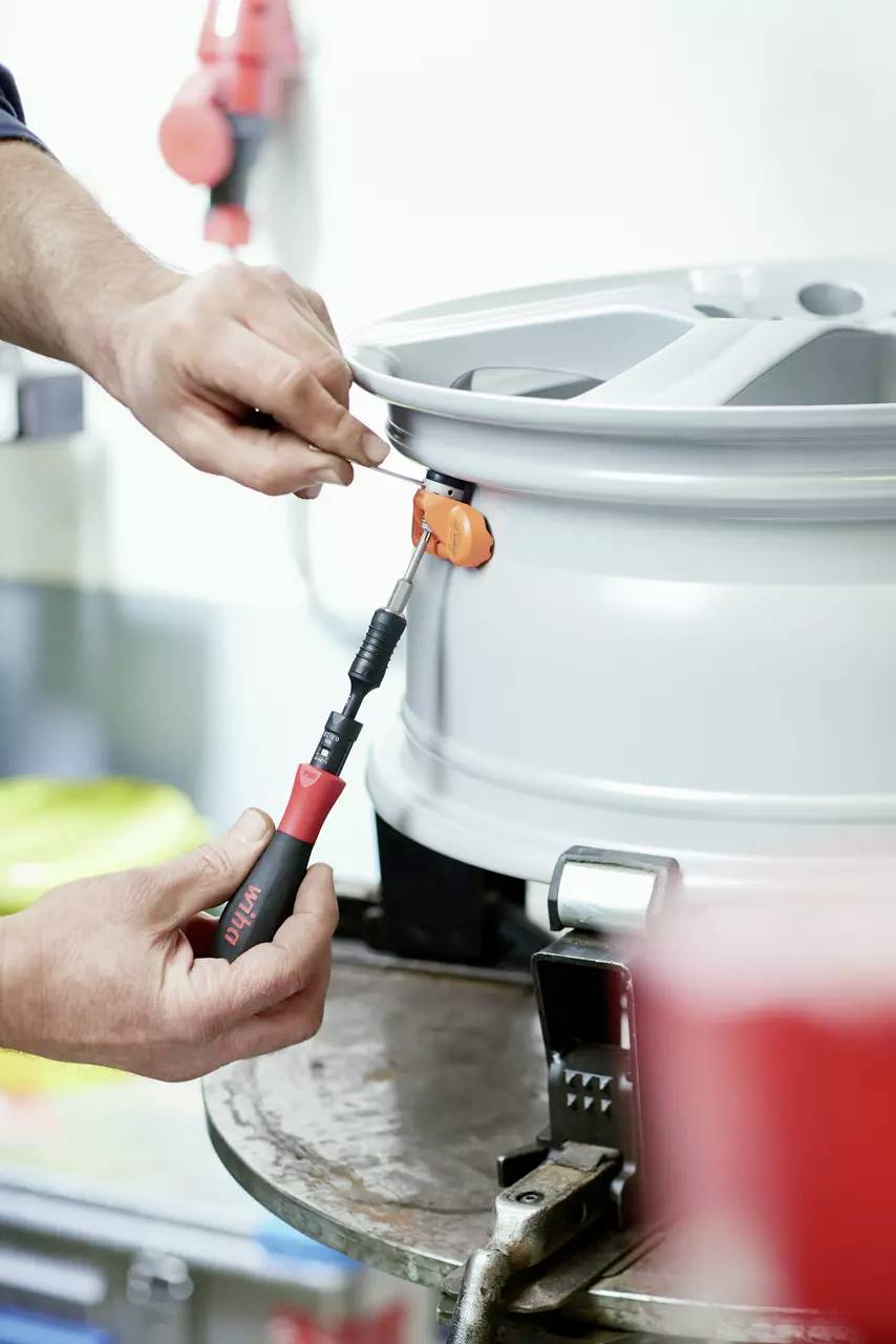 Person montiert Reifen auf Felge mit Schraubenschlüssel in Autowerkstatt. Fokussiert auf handwerkliche Tätigkeit und Werkzeug.