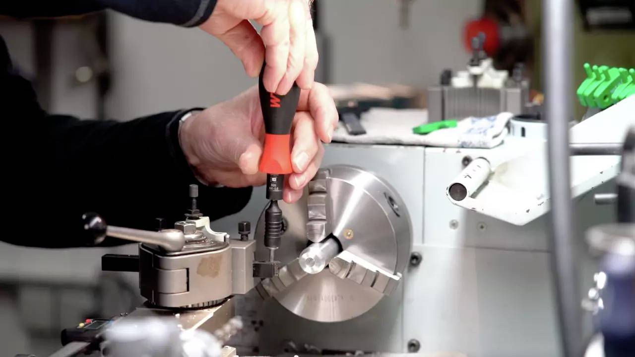 Eine Person verwendet einen Schraubenzieher, um eine Metallmaschine einzustellen. Hände in Aktion. Präzise Feinmechanik-Arbeit.