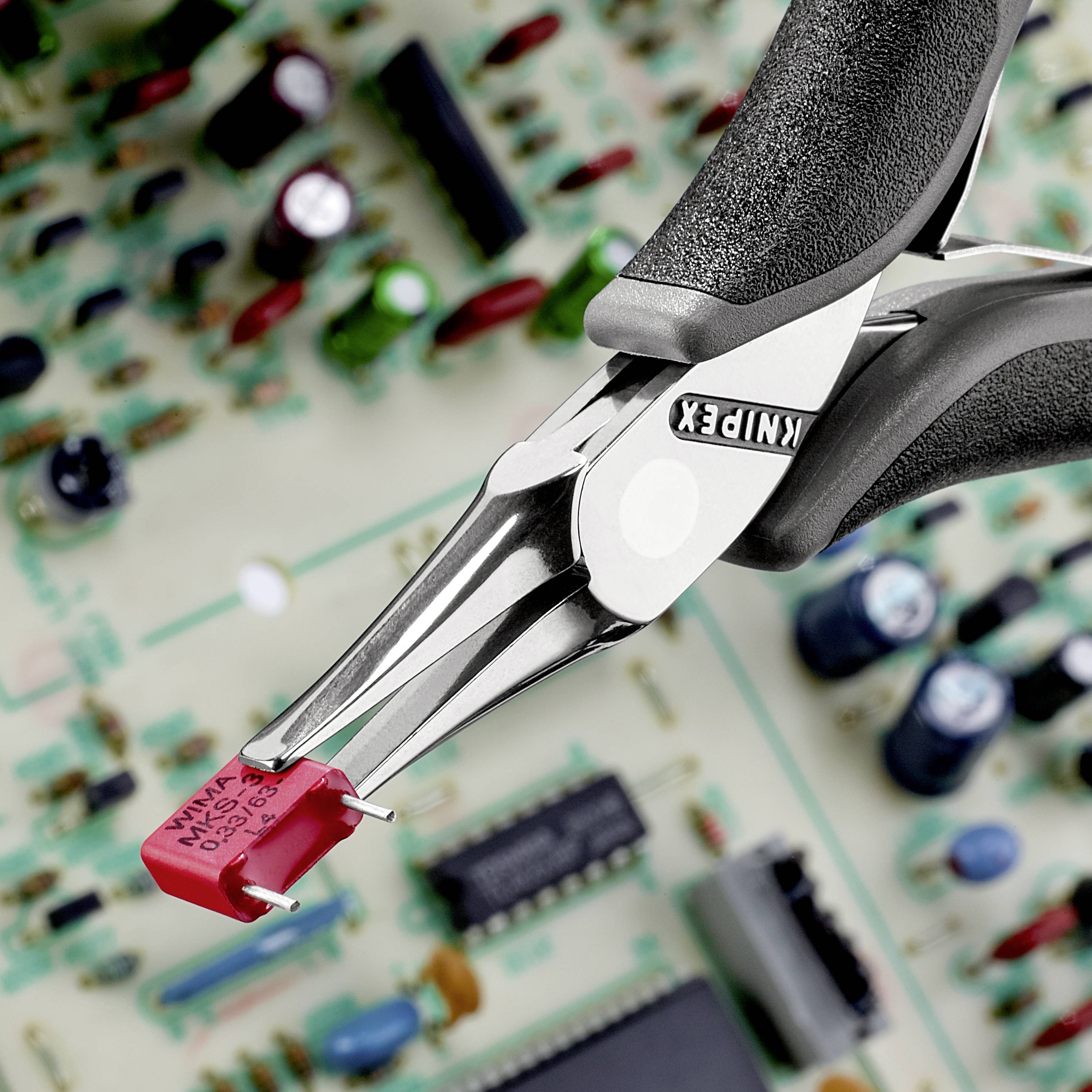 Spitzzange hält roten elektronischen Widerstand auf einer Platine. Im Hintergrund unscharfe elektronische Bauteile.