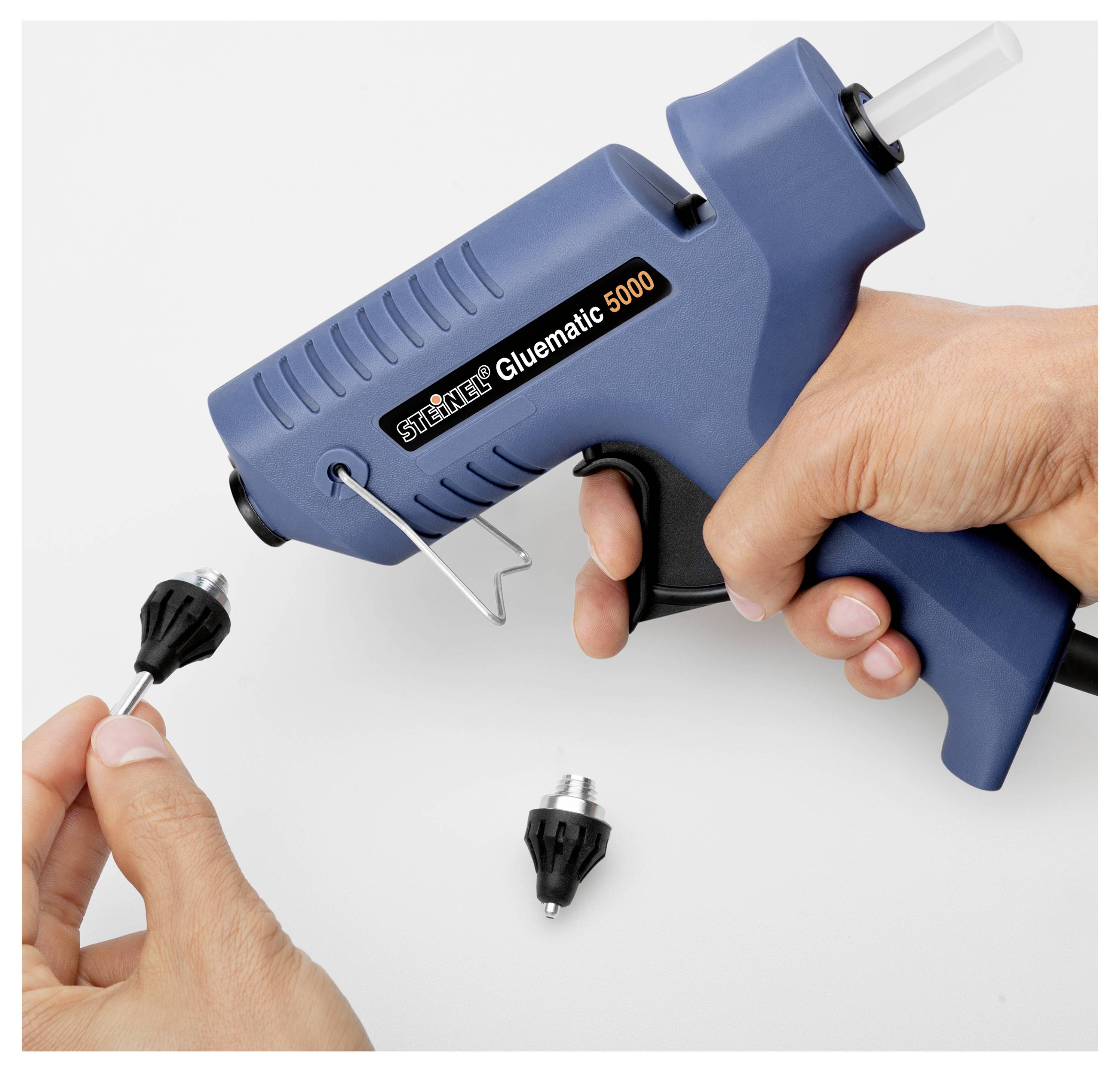 Hände, die eine blaue Heißklebepistole mit der Bezeichnung "Steinel Gluematic 5000" verwenden, um Kleber auf eine kleine schwarze Düse auf einer weißen Oberfläche aufzutragen.