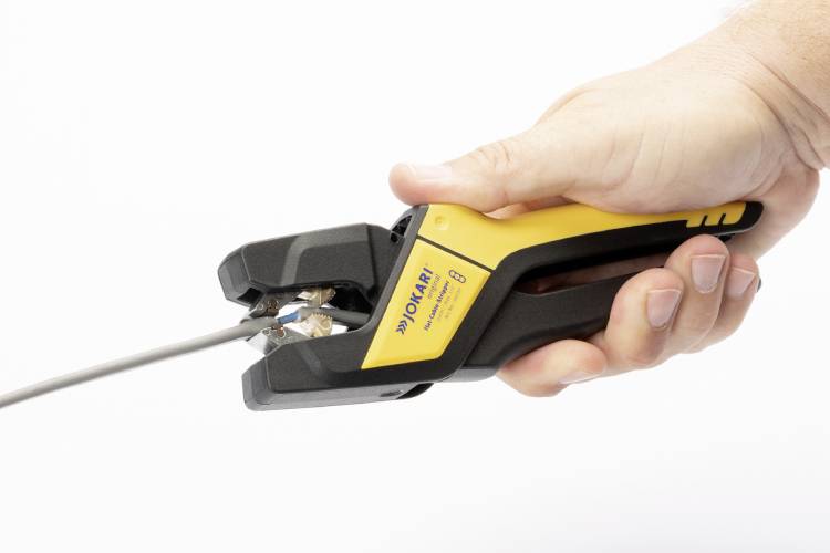 Eine Hand hält ein Abisolierwerkzeug, das ein Kabel bearbeitet. Das Werkzeug ist schwarz und gelb und wird fest um das Kabel geschlossen.