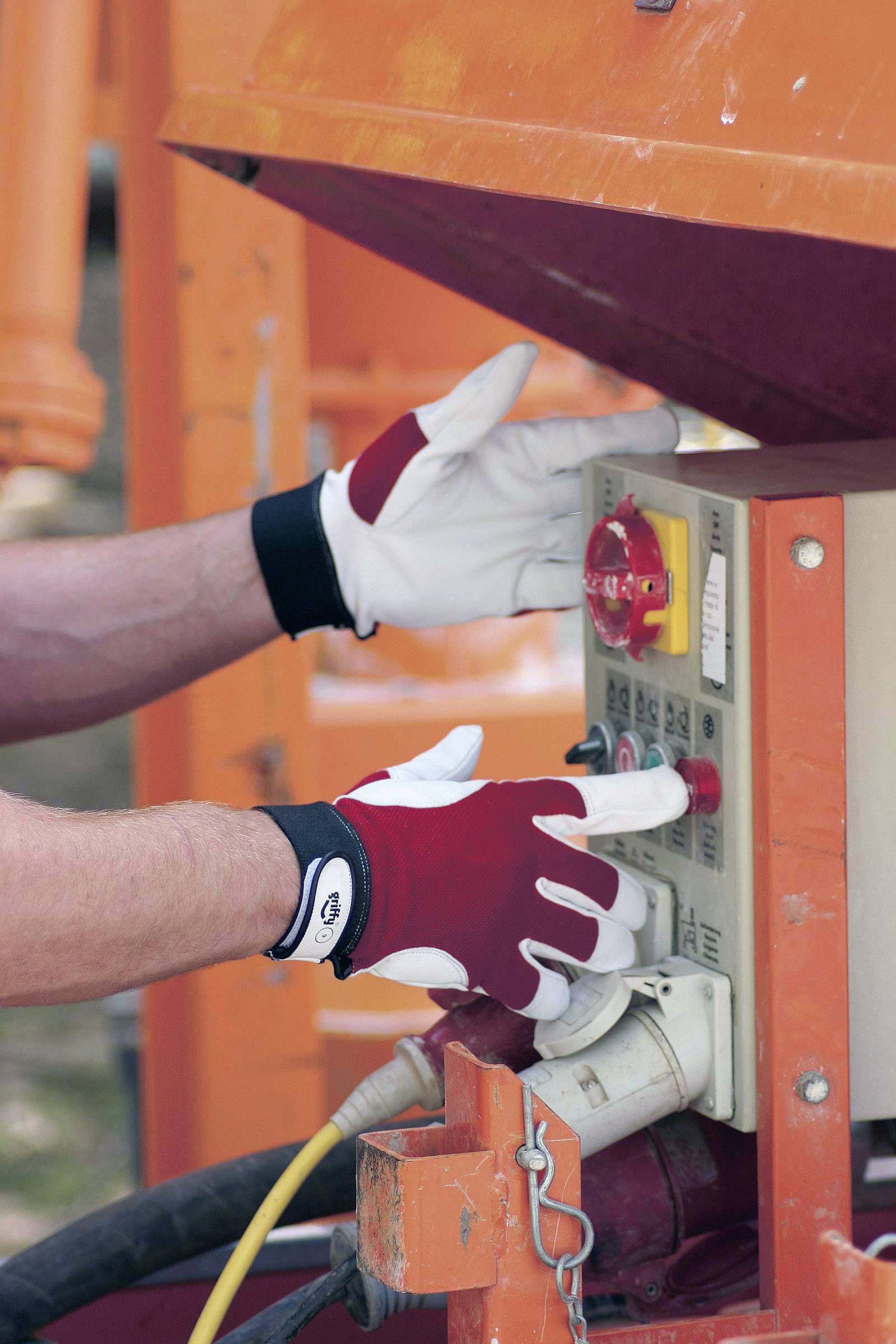 Eine Person in Arbeitshandschuhen bedient ein Kontrollpanel mit Knöpfen und Schaltern an einer orangefarbenen Maschine im Freien.